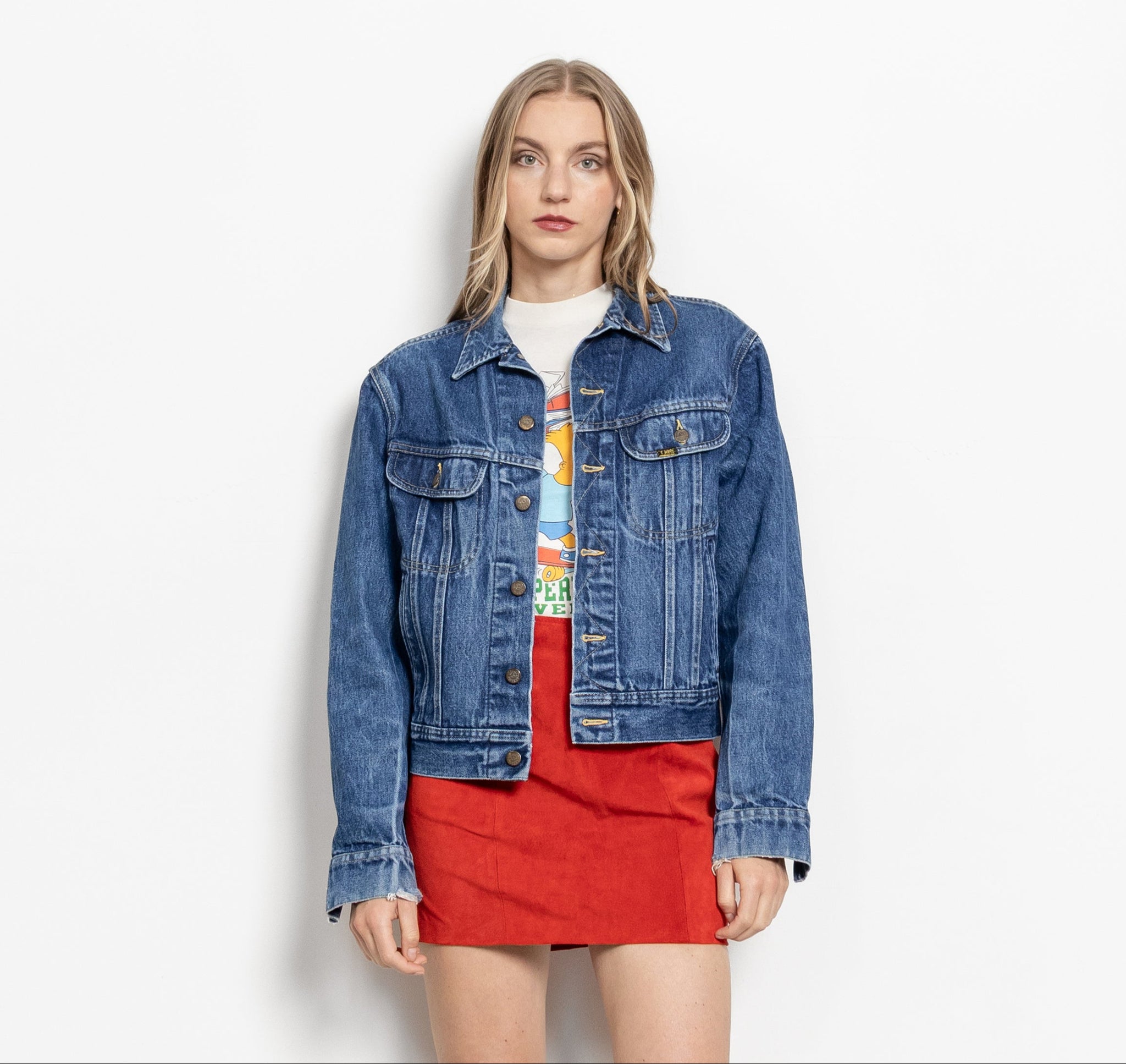 A woman wearing a vintage Lee dark wash blue denim jacket over a red dress, with the jacket's sleeves rolled up to the elbows.