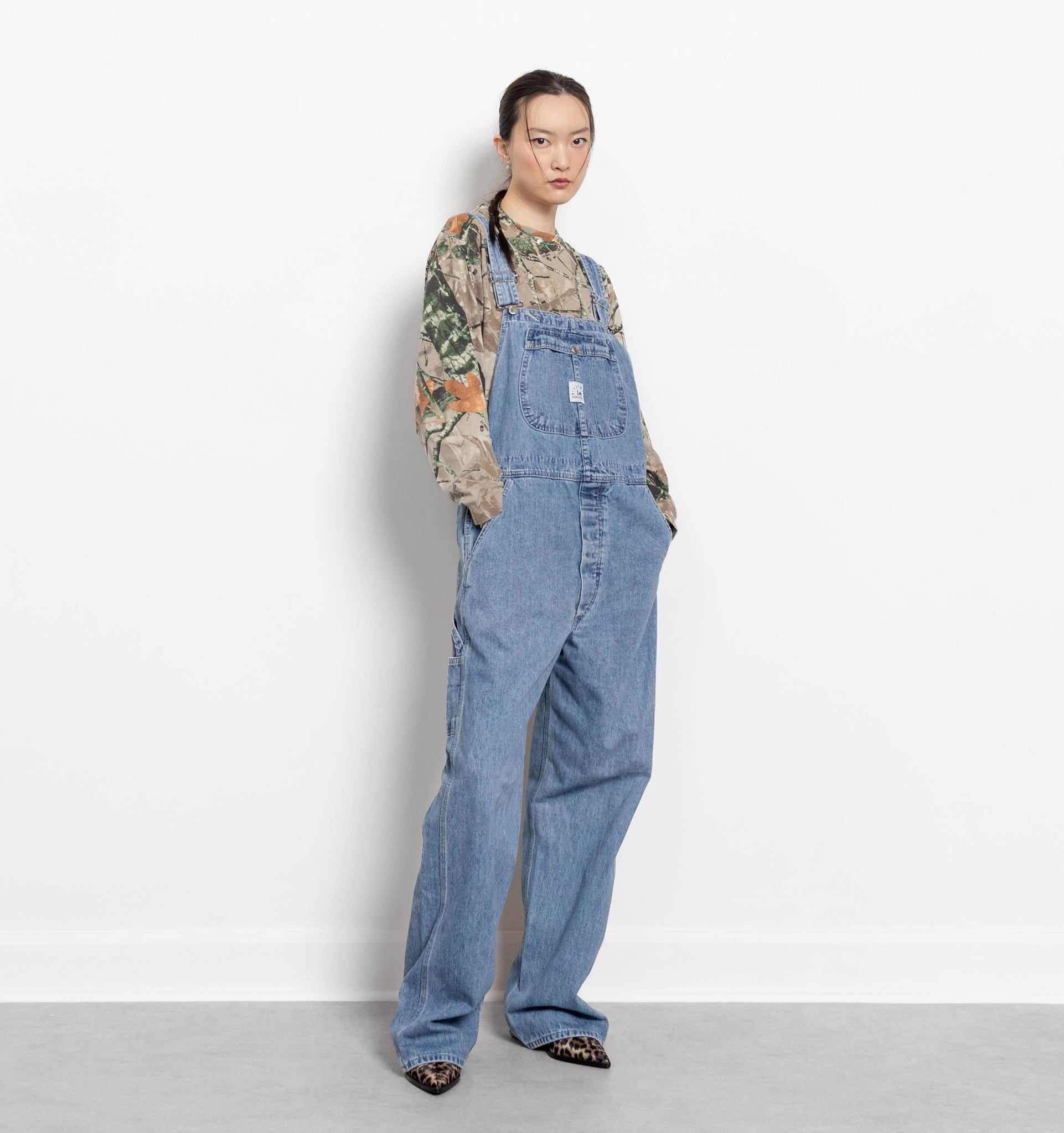 Person wearing blue denim overalls and a patterned shirt on a white background