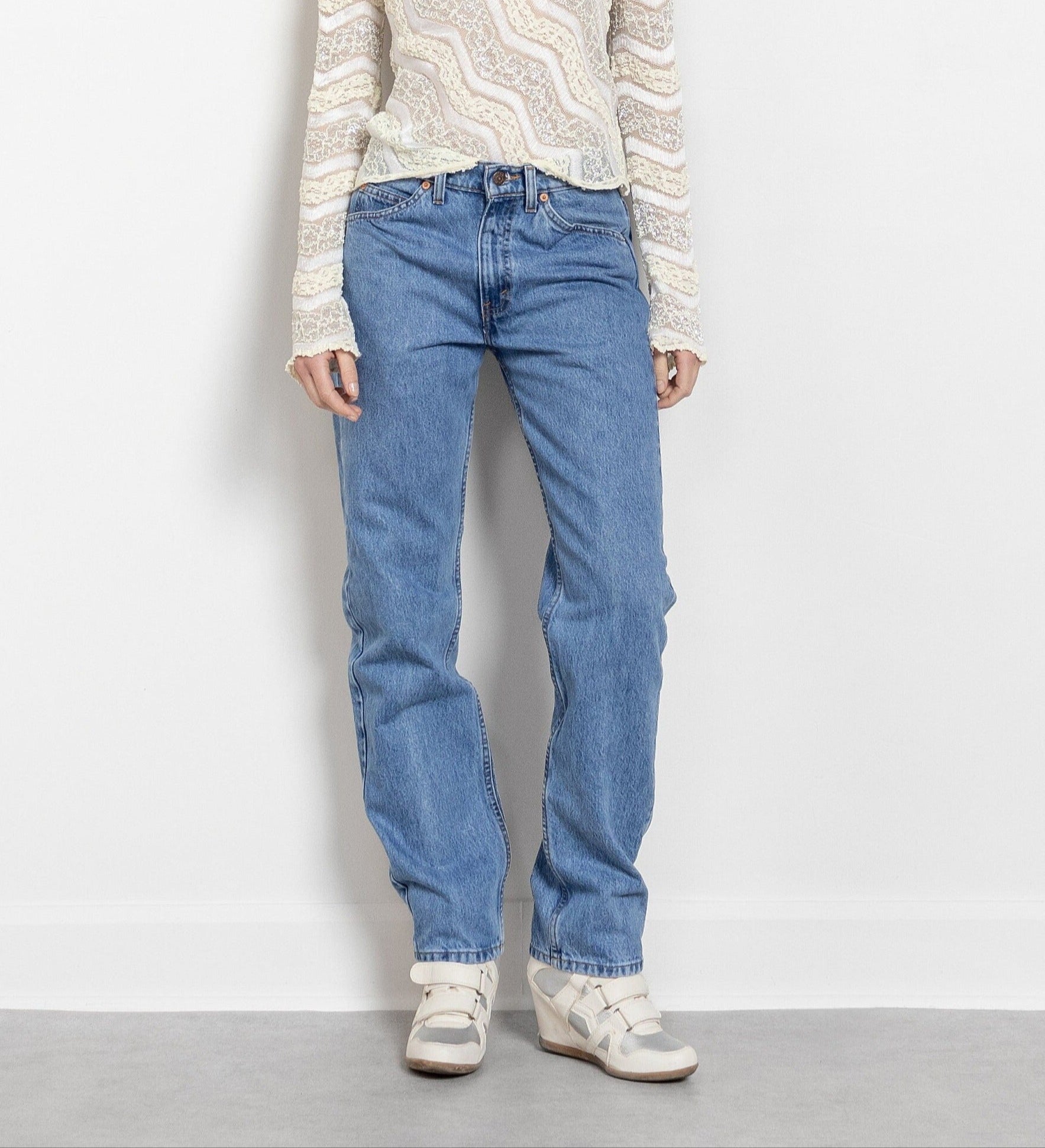 A person standing against a white background, wearing vintage Levi's jeans and a long-sleeved top with a geometric pattern.