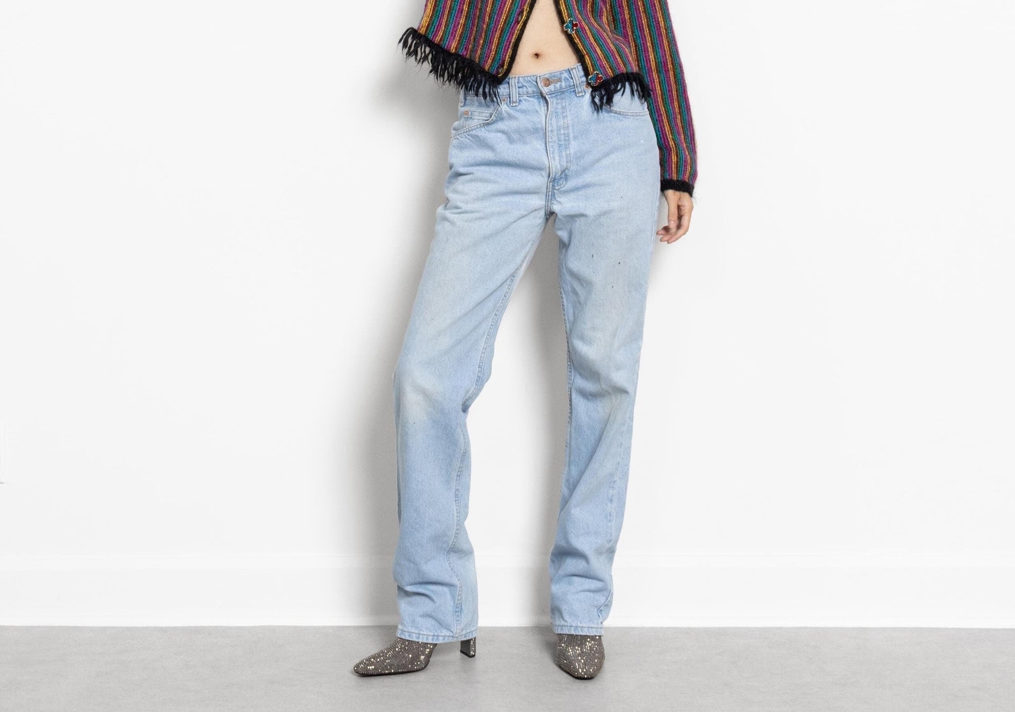 A person standing against a white background wearing vintage Levi's jeans with a high waist and tapered leg, along with a multicolored top and boots.