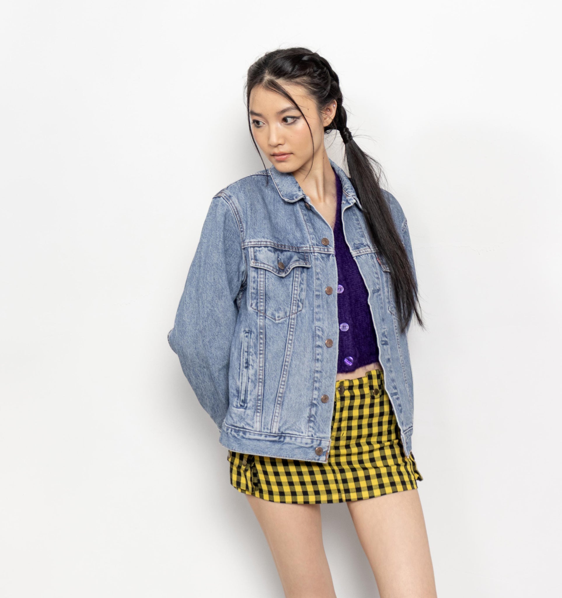Woman wearing a denim jacket, purple top, and yellow checkered skirt on a white background