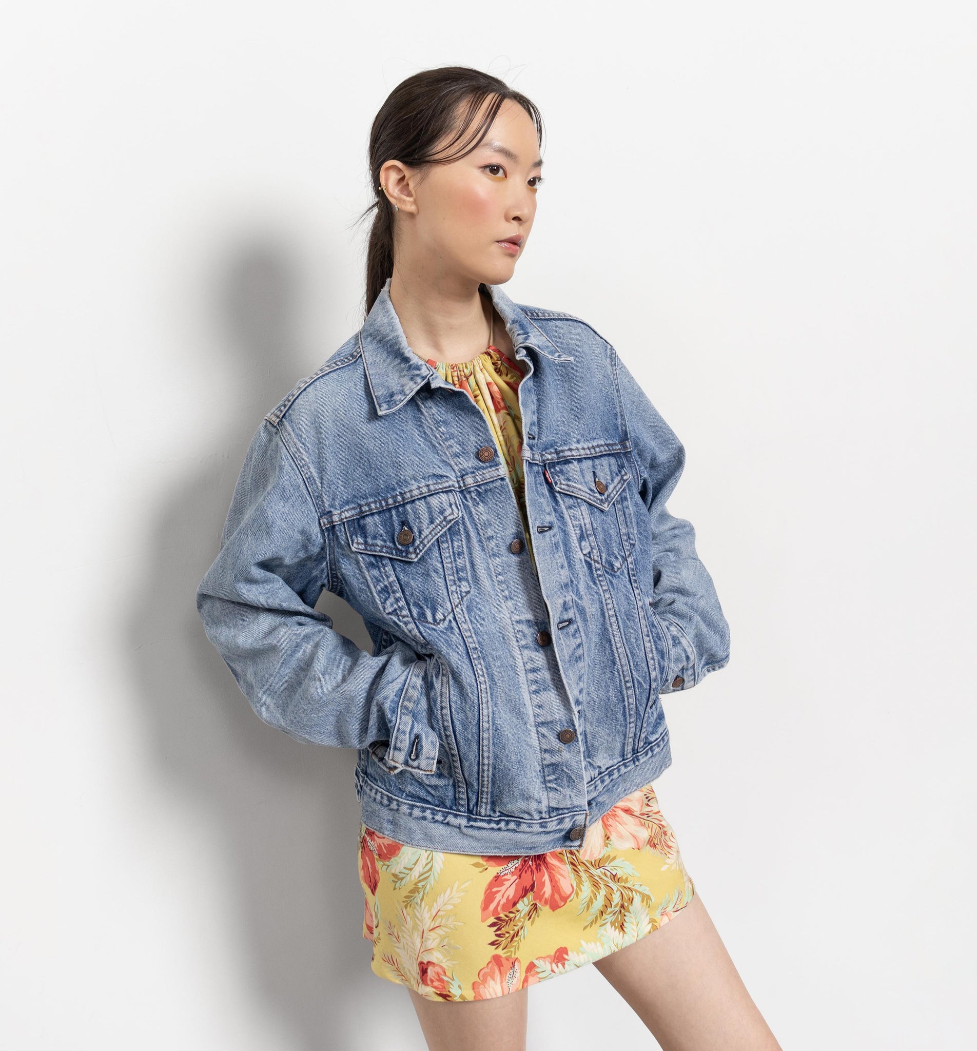 Woman wearing a denim jacket over a floral dress on a white background