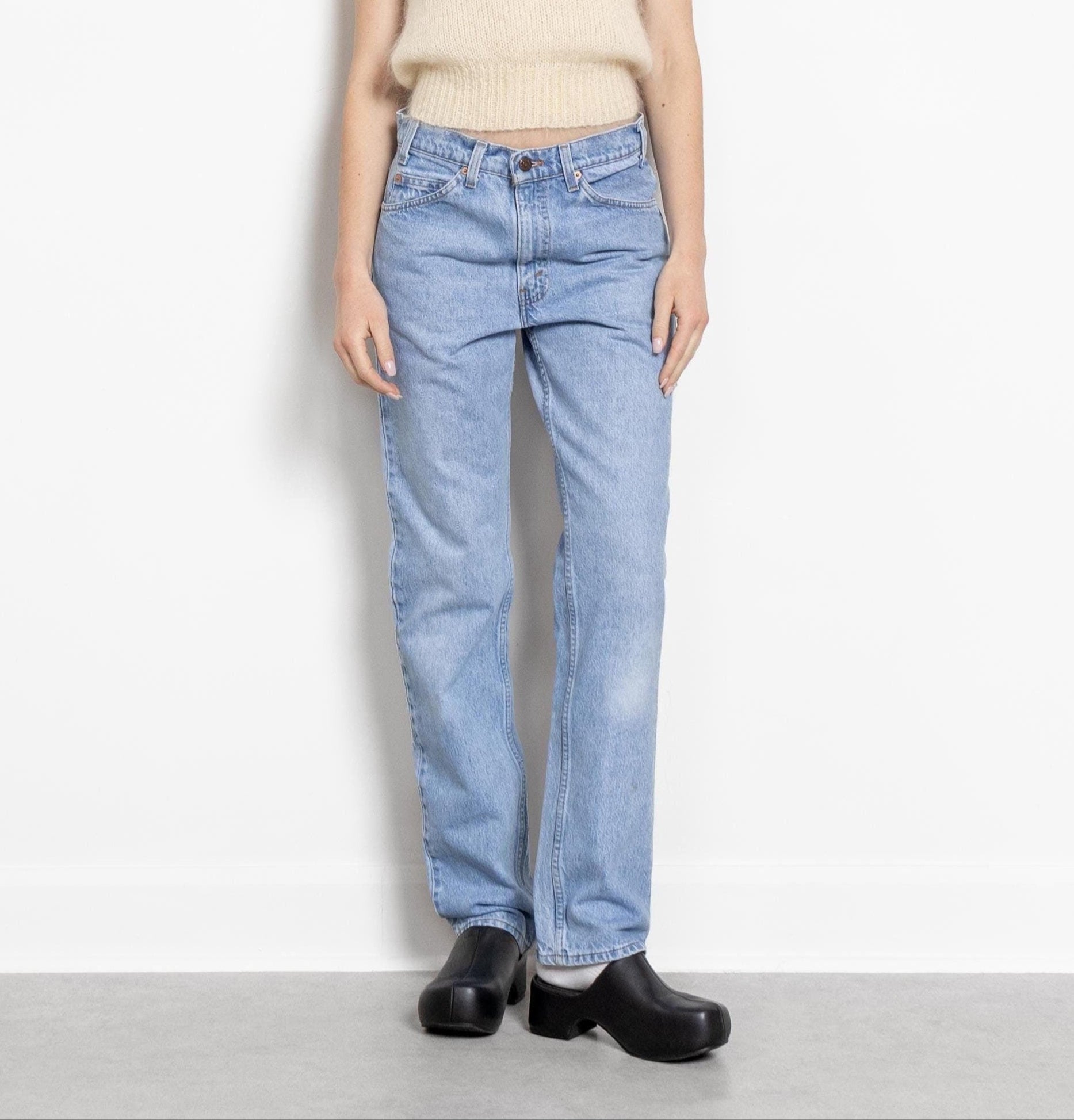 A person standing against a white background, wearing high-waisted, straight leg Levi's 509 boyfriend jeans with a zip fly, in a medium wash with visible fading. The person is also wearing a beige sweater and black shoes.