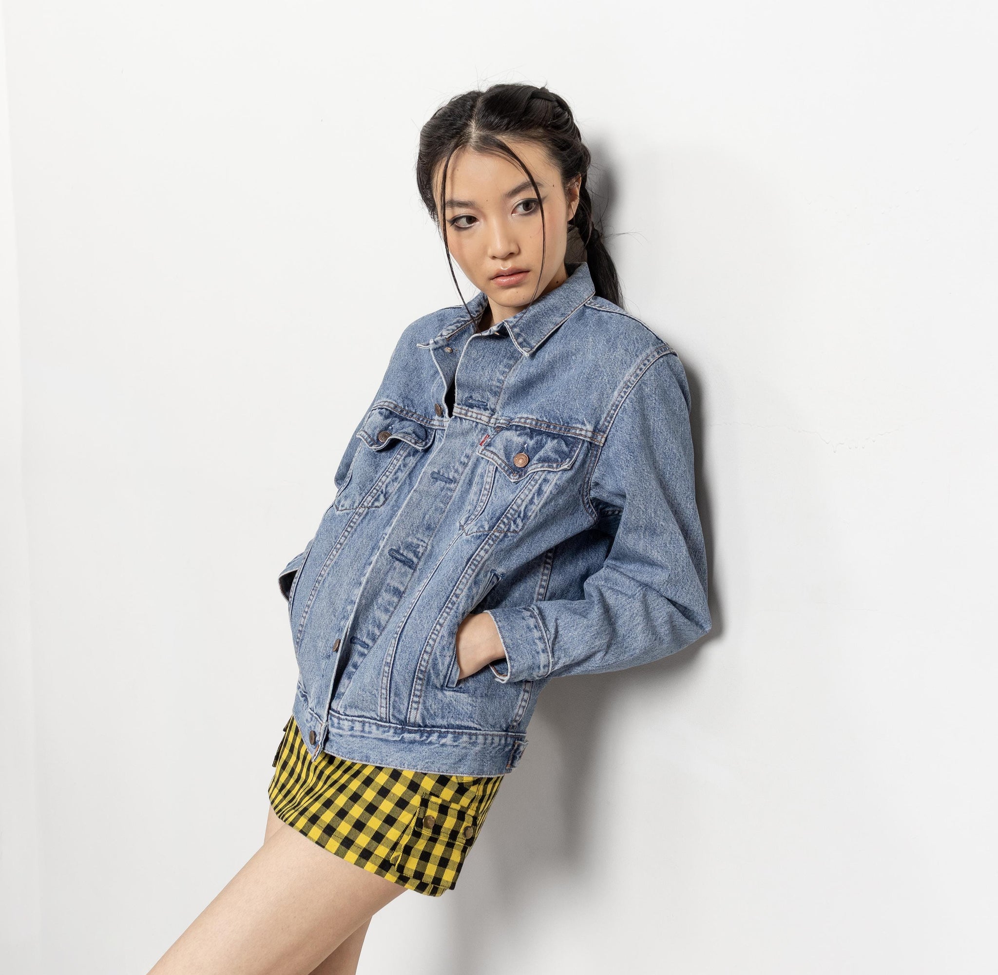 Woman wearing a denim jacket and yellow checkered skirt against a white background