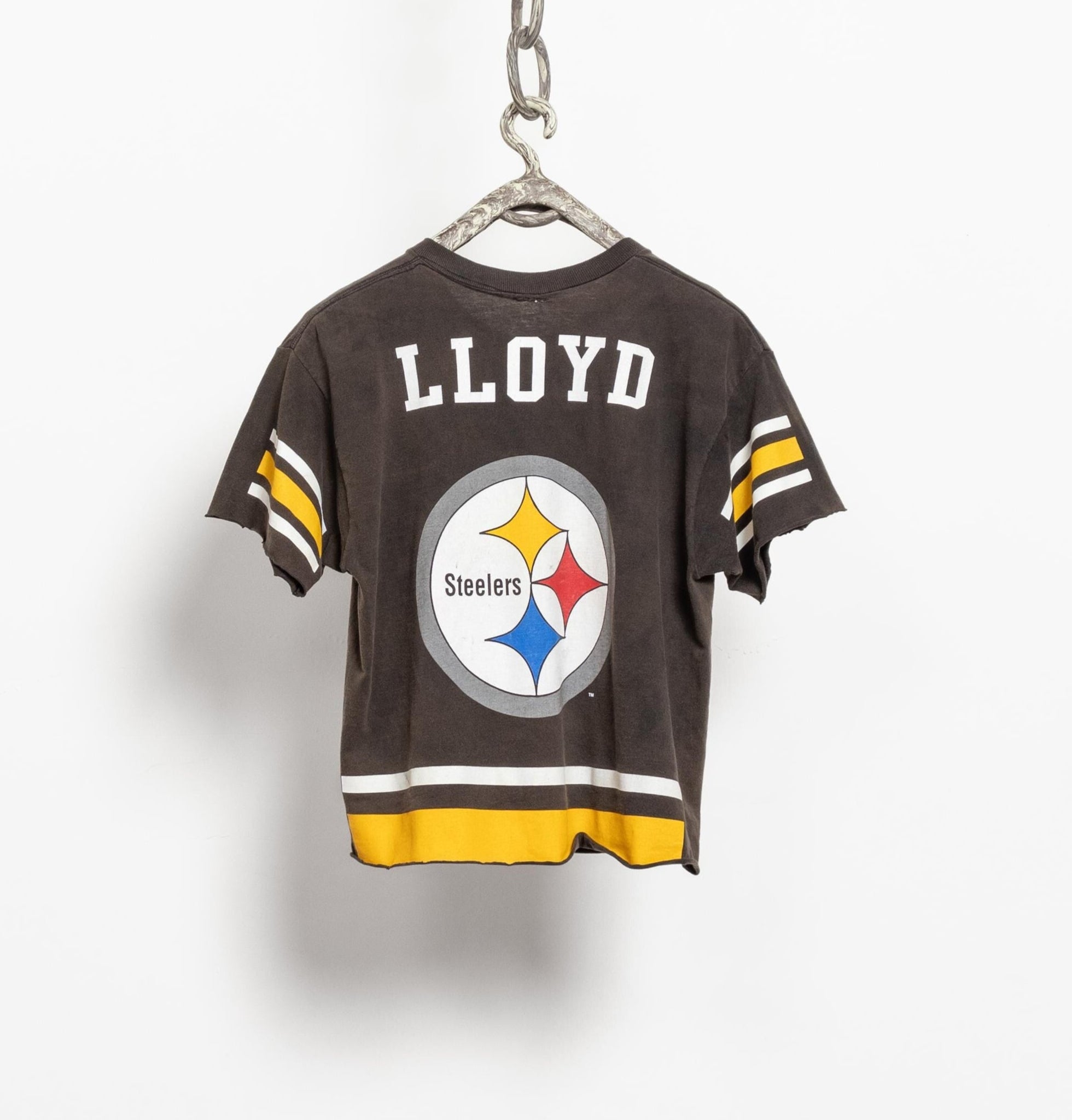 A vintage 90's NFL Pittsburgh Steelers short sleeve jersey in brown, with the Steelers logo on the front and additional Steelers logos on the shoulders. The jersey is displayed on a white background.