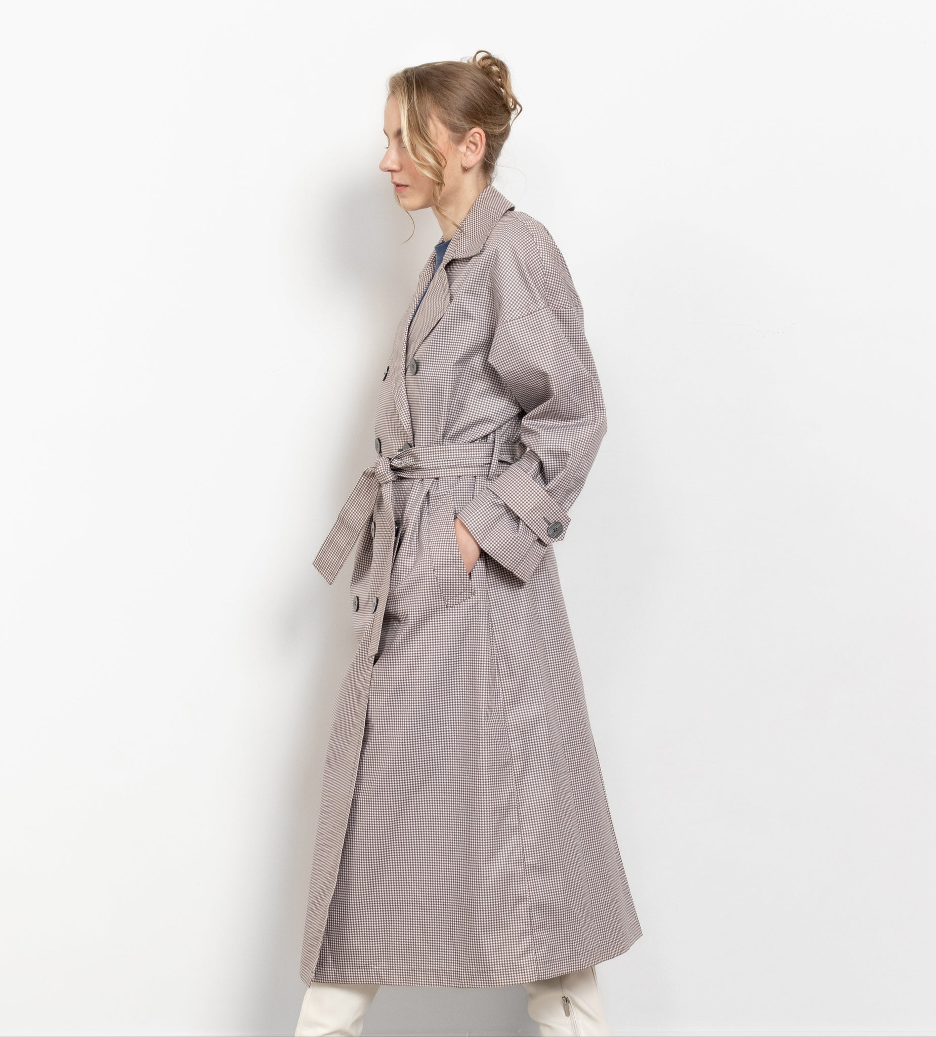 Woman wearing a long gray trench coat and white boots on a plain background
