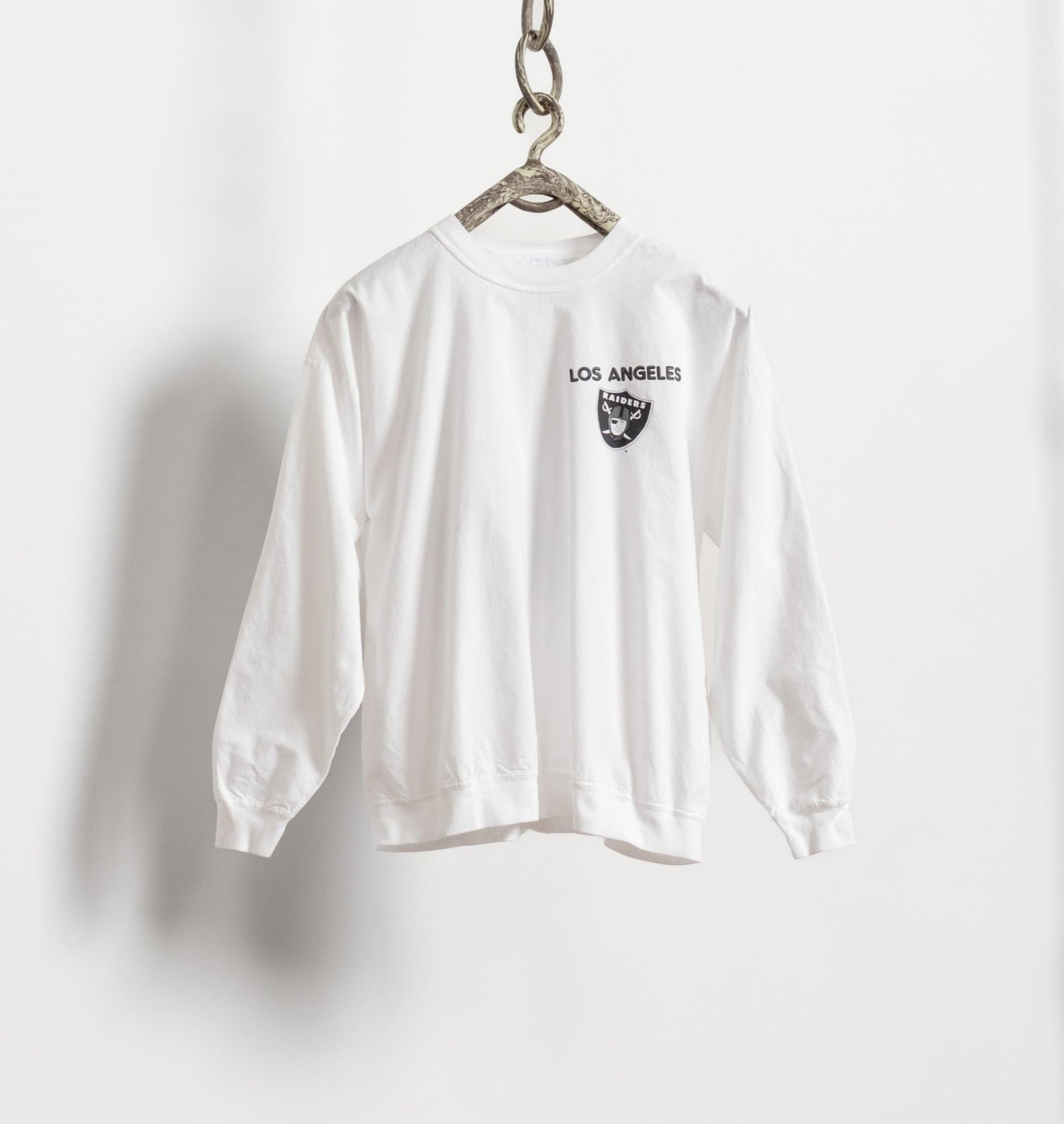 White long-sleeve shirt with 'Los Angeles' print on a hanger against a white background