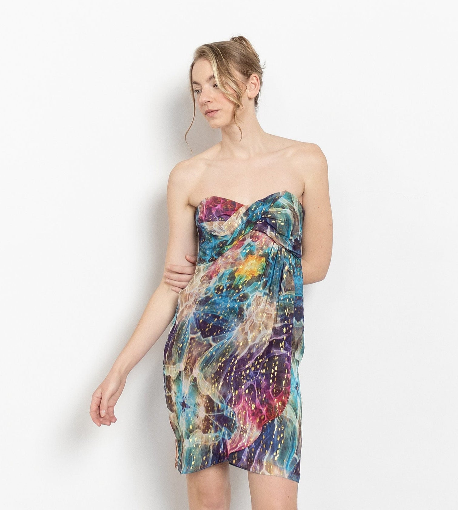 A woman wearing a strapless, metallic gold dots patterned midi dress with a sweetheart neckline and layers of sheer rainbow silk.