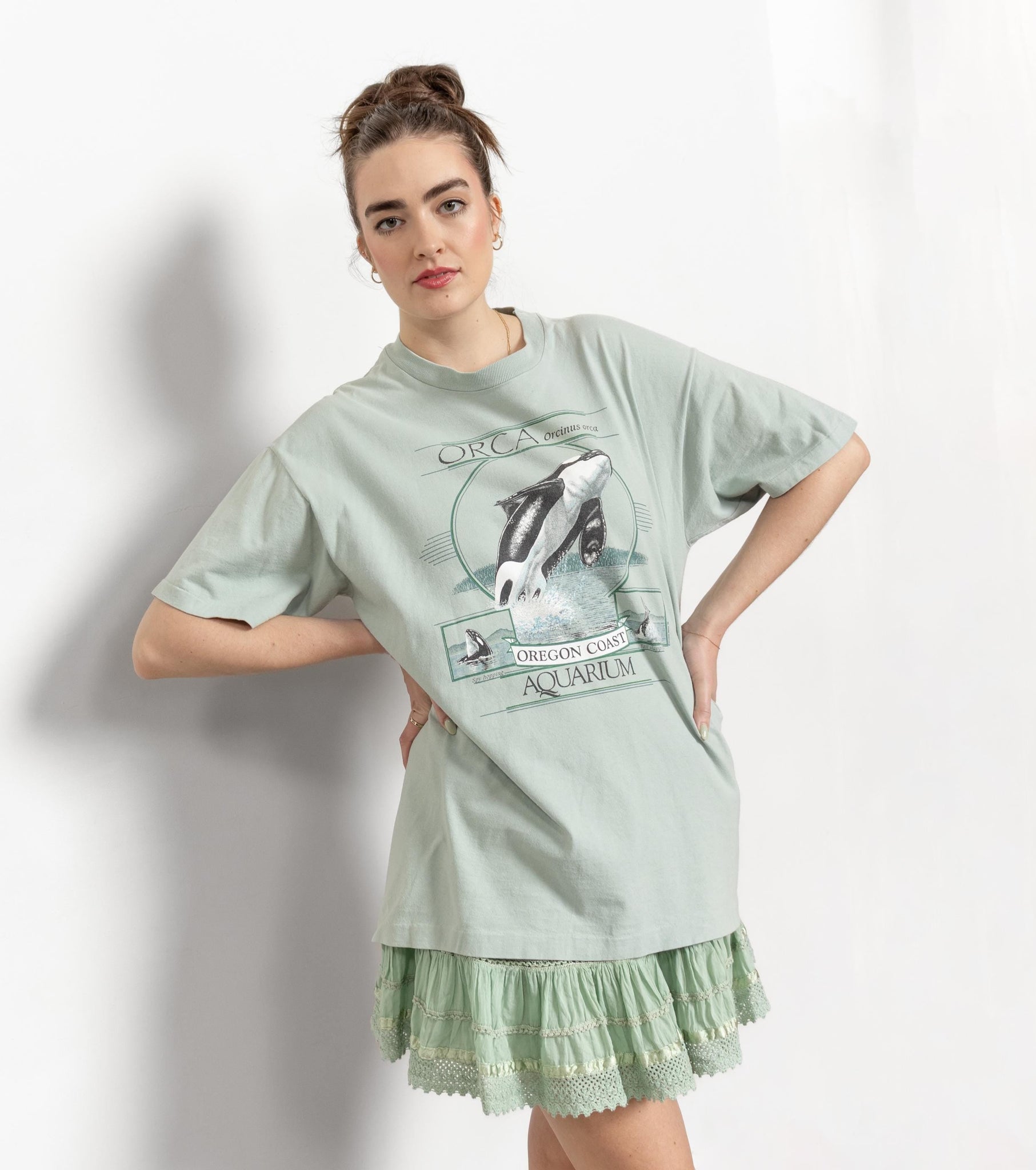 Woman wearing a light green oversized t-shirt with a graphic design on a white background