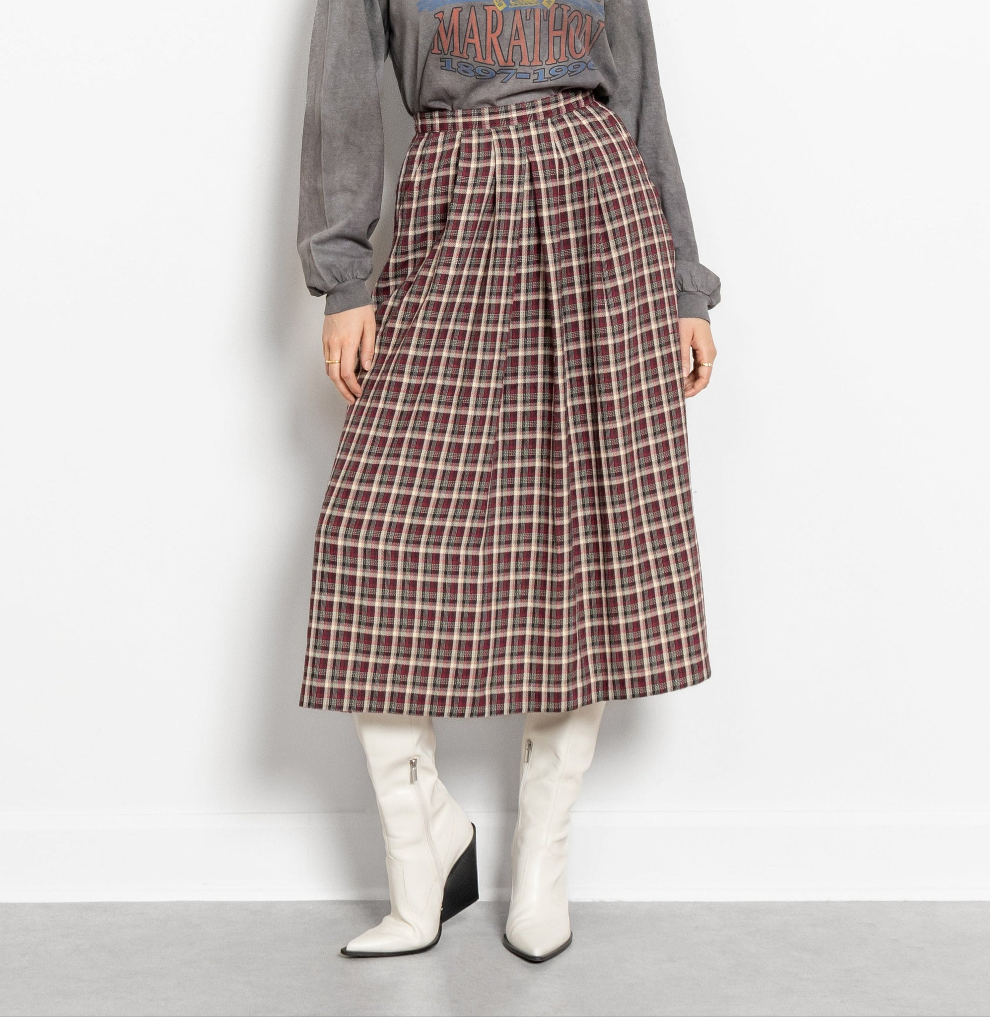 Person wearing a plaid skirt and gray sweater on a plain background