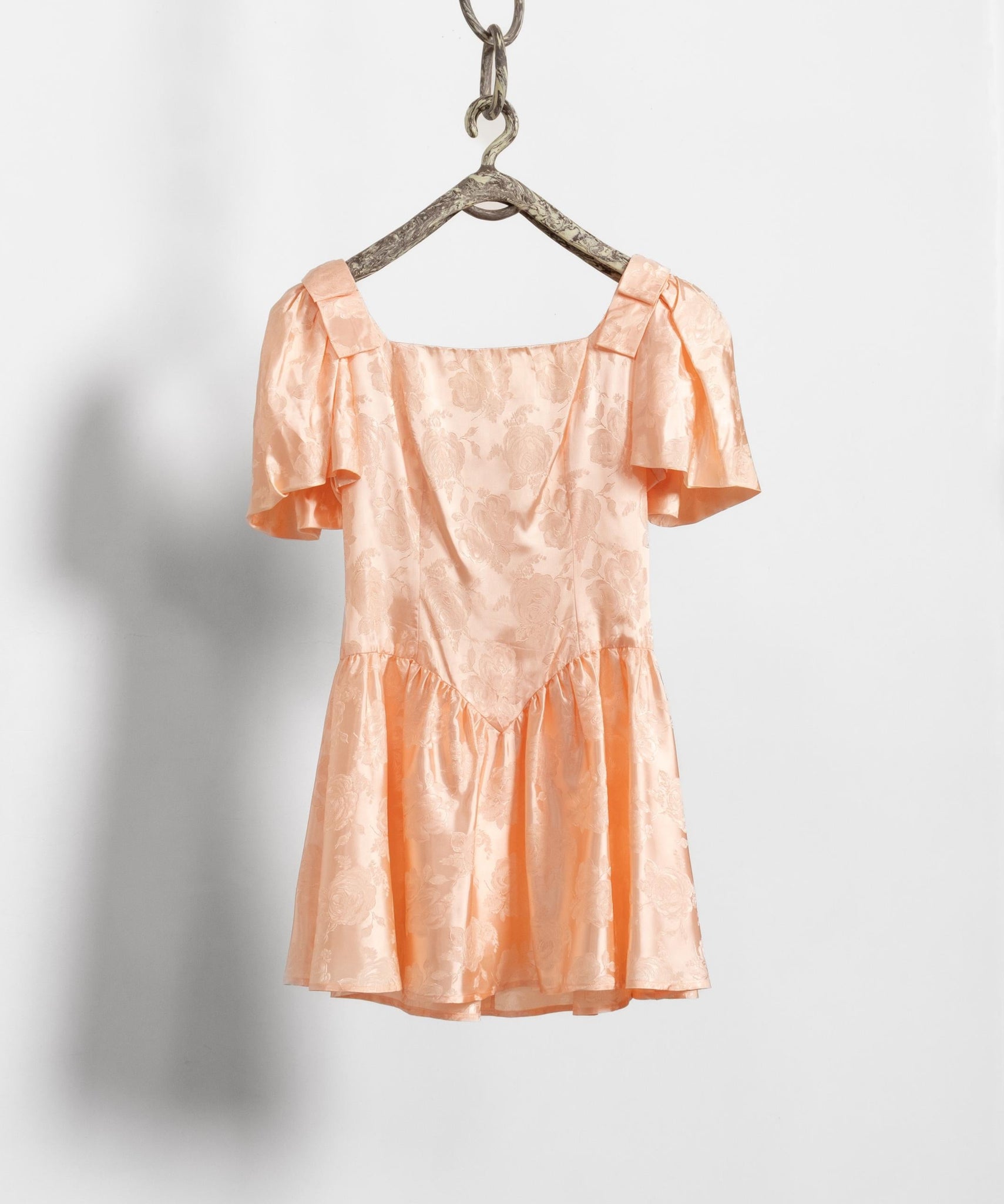 Peach-colored dress hanging on a hook against a white background