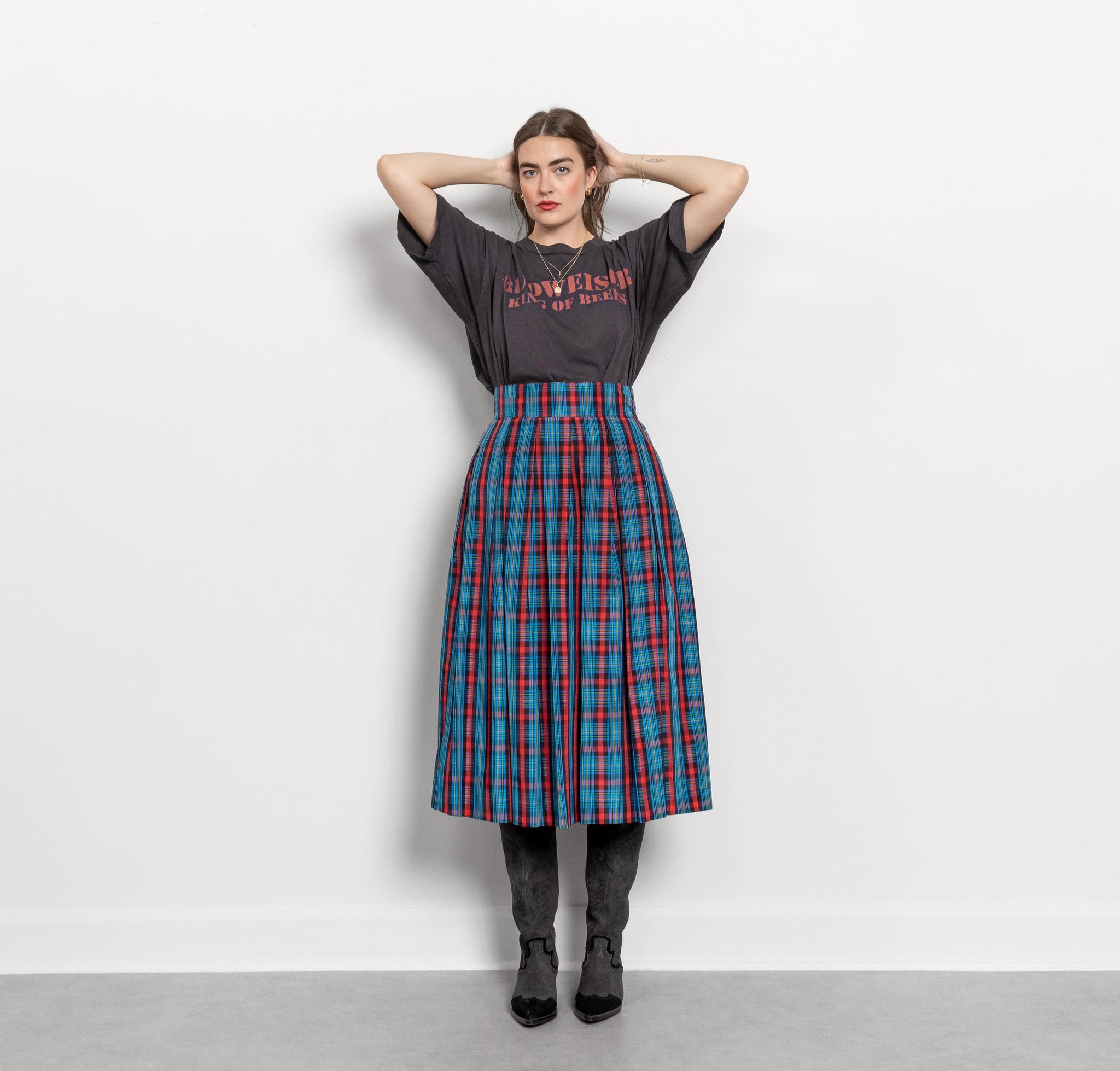Person wearing a black t-shirt with text and a blue plaid skirt on a white background