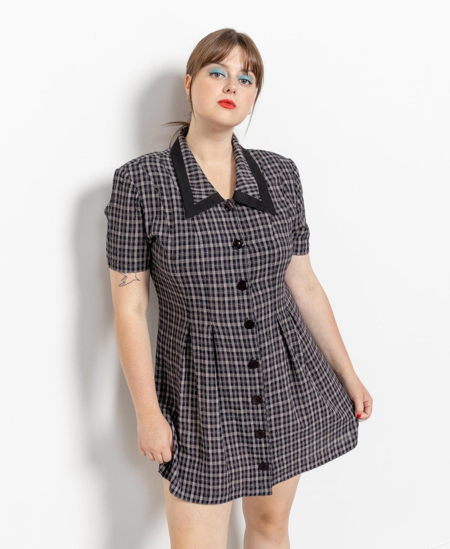 A woman modeling a vintage 90's black and grey checkered mini dress with a collar and buttons down the front.
