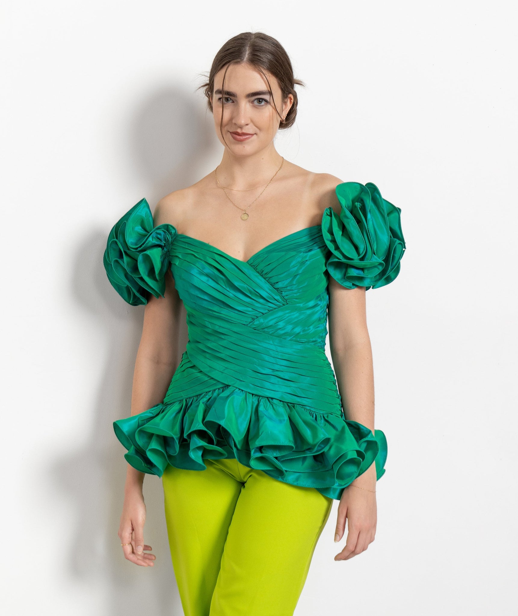 Woman wearing a green off-shoulder top with ruffled details and green pants on a white background