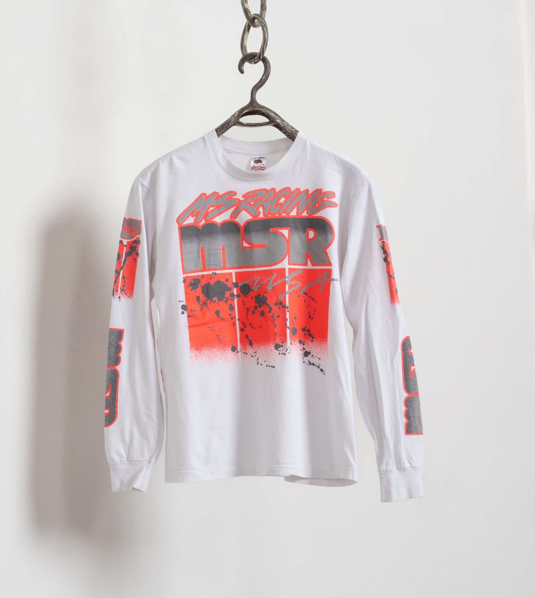 A long sleeve white cotton t-shirt with vibrant red and pink graphics and text, hanging on a hanger against a white background.
