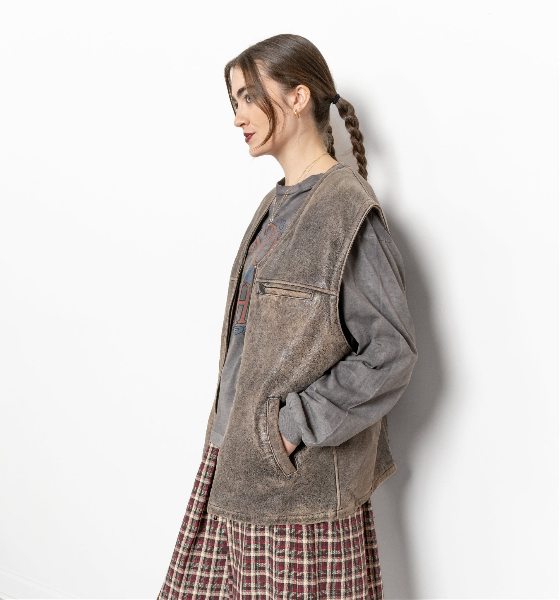 Woman wearing a gray jacket and plaid skirt against a white wall