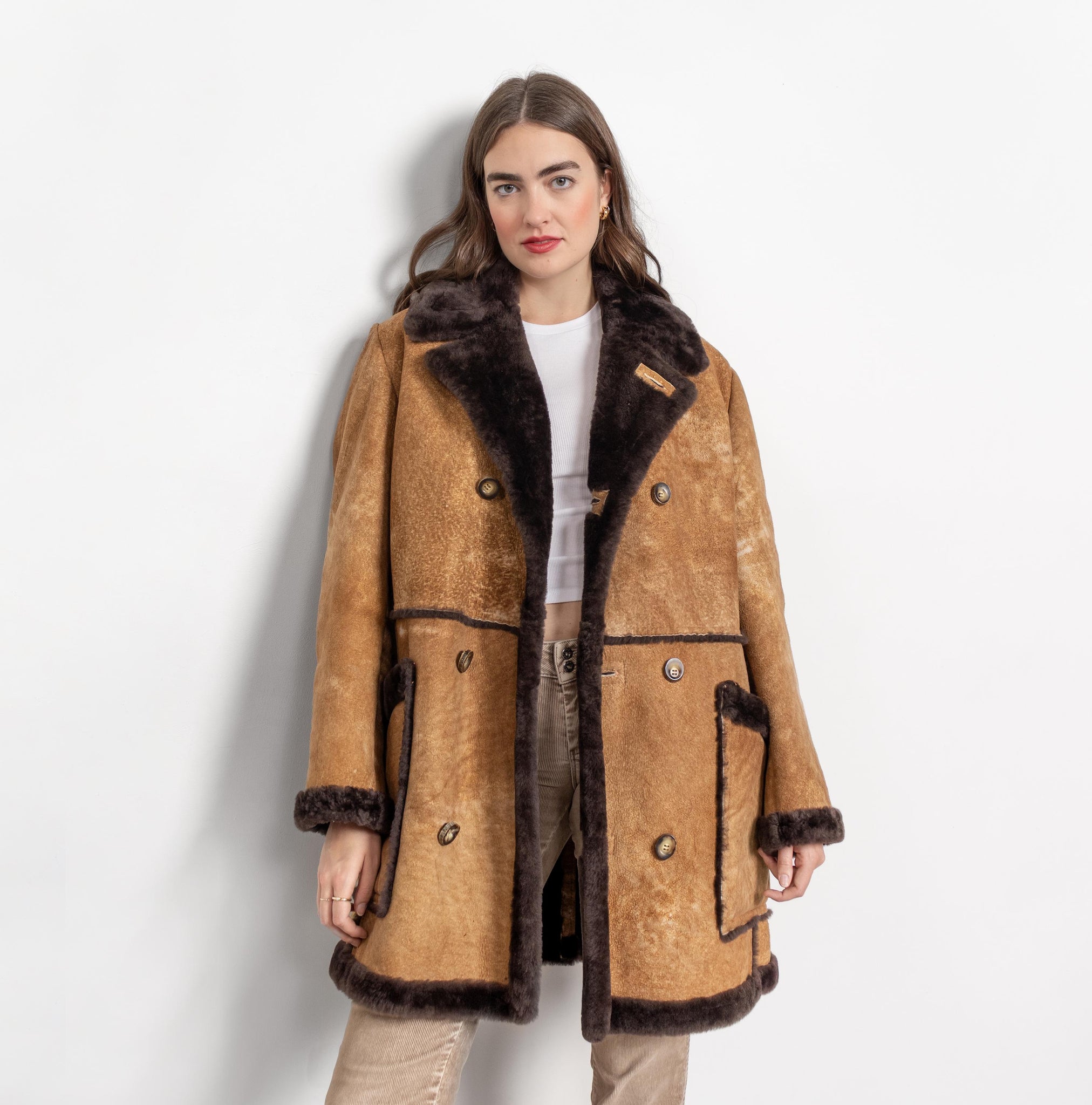 Woman wearing a brown shearling coat with fur trim on a white background