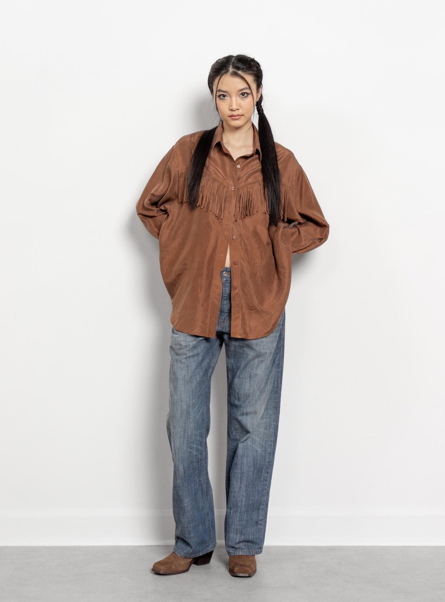 Person wearing a brown fringed shirt and blue jeans against a white background