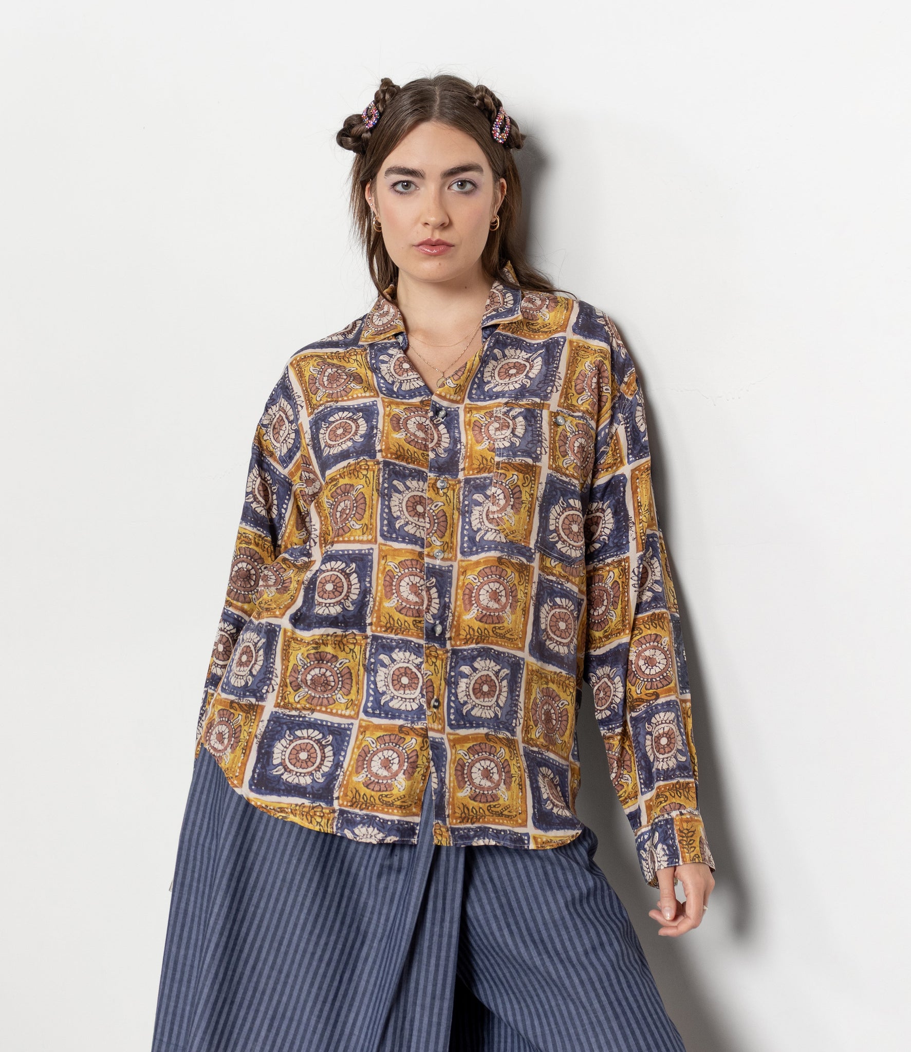 Woman wearing a patterned shirt and blue skirt against a white background