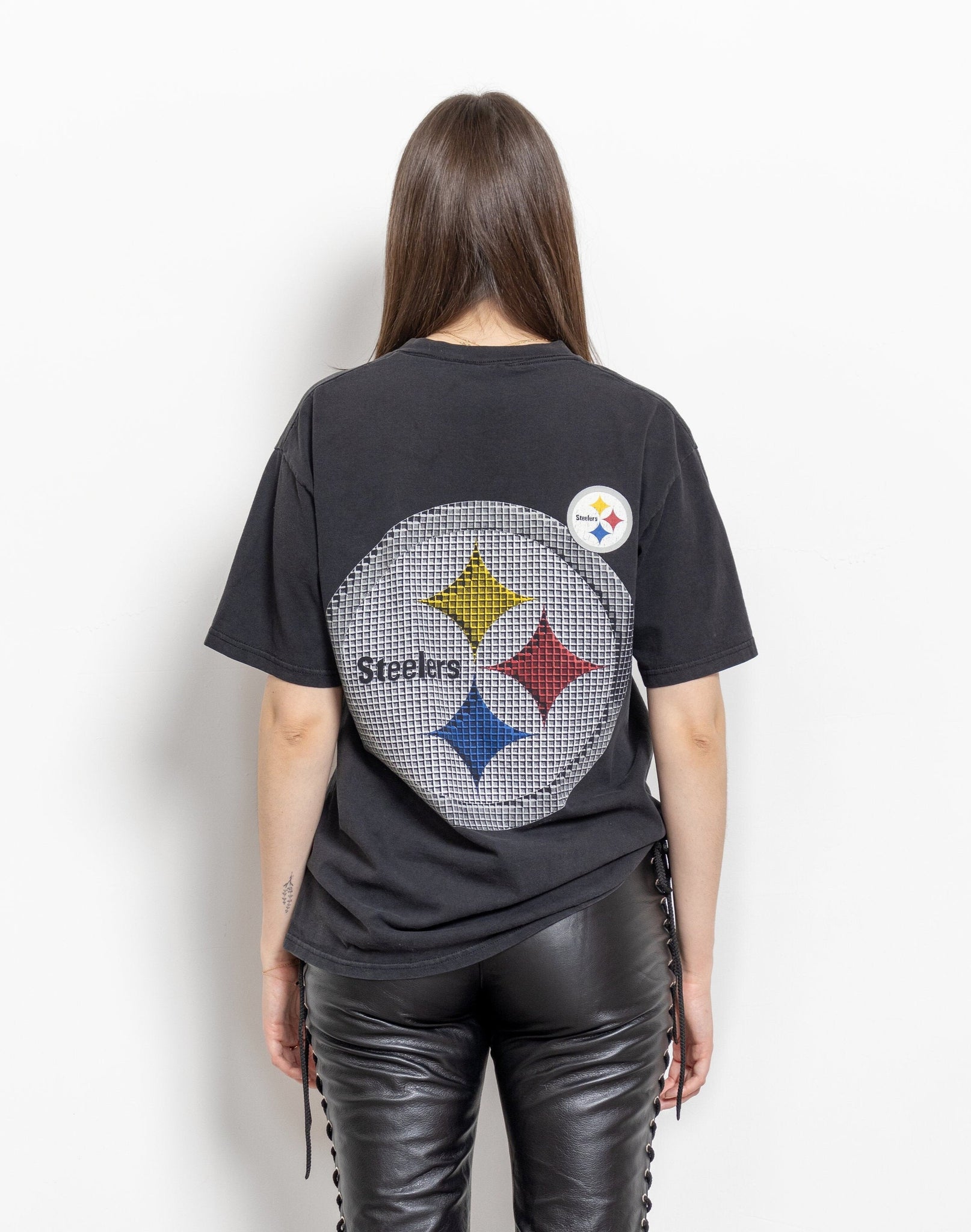 A person wearing a vintage 90's NFL Pittsburgh Steelers short sleeve tee with a large graphic of the Steelers logo on the back.