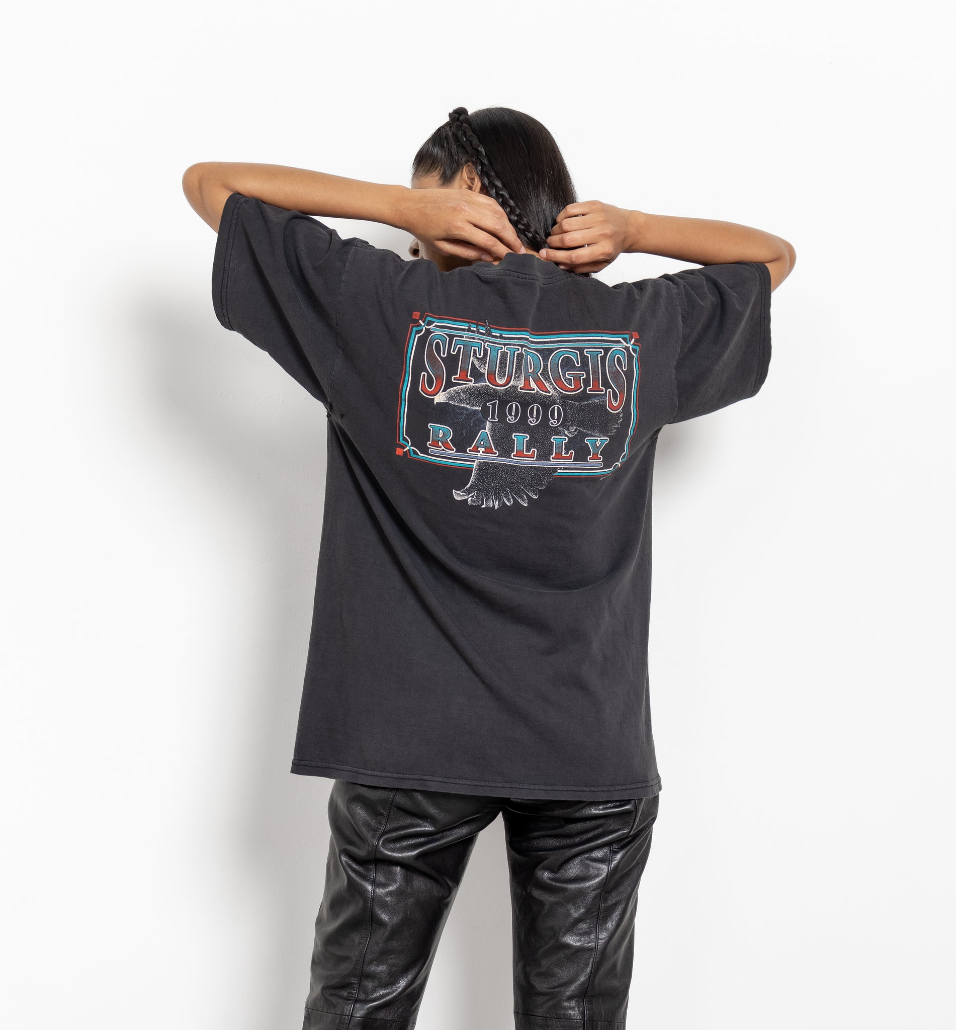 A person wearing a vintage black t-shirt with 'Sturgis 1999' text and graphics on the back.