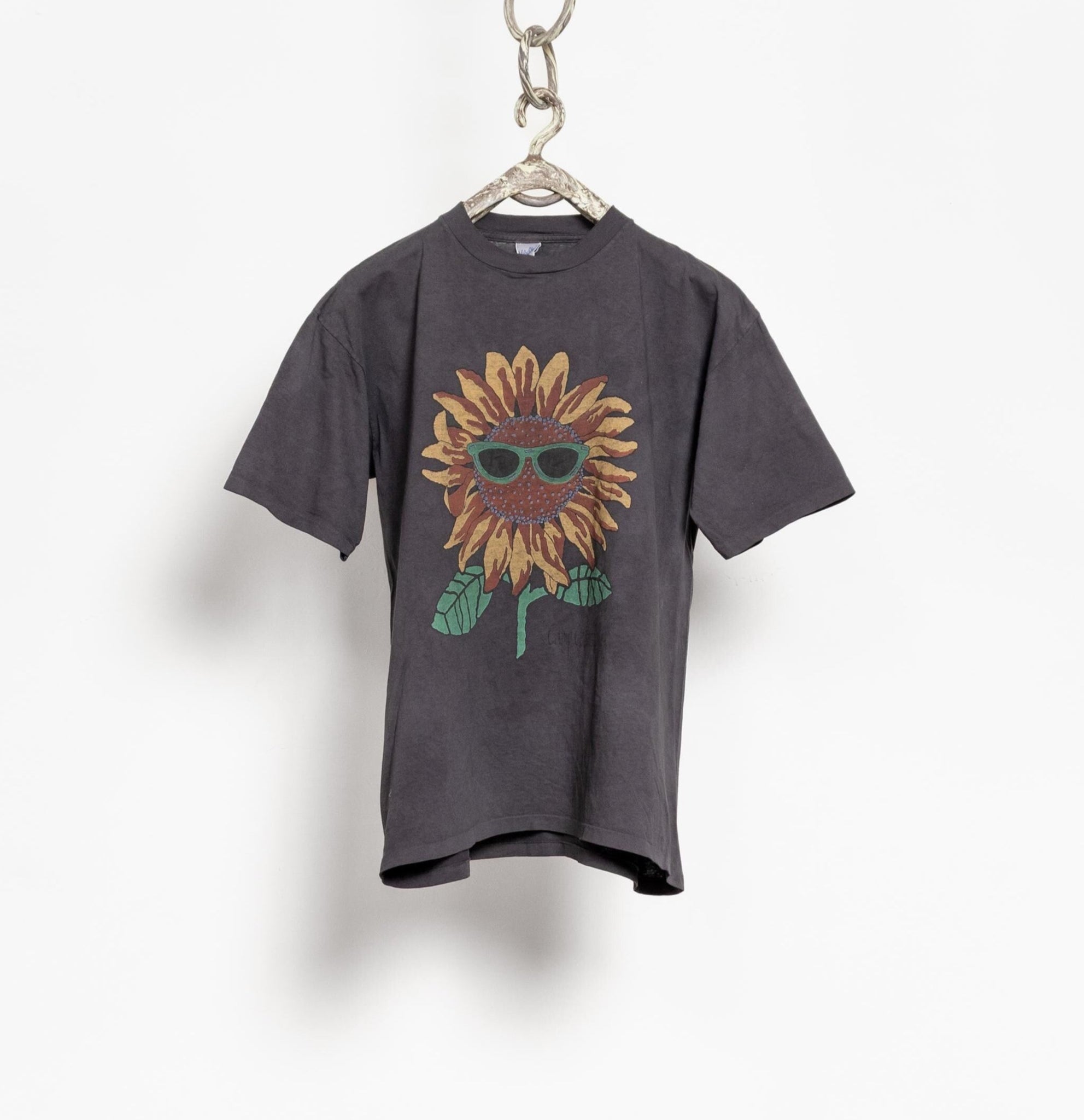 Gray t-shirt with a sunflower design wearing sunglasses on a hanger against a white background