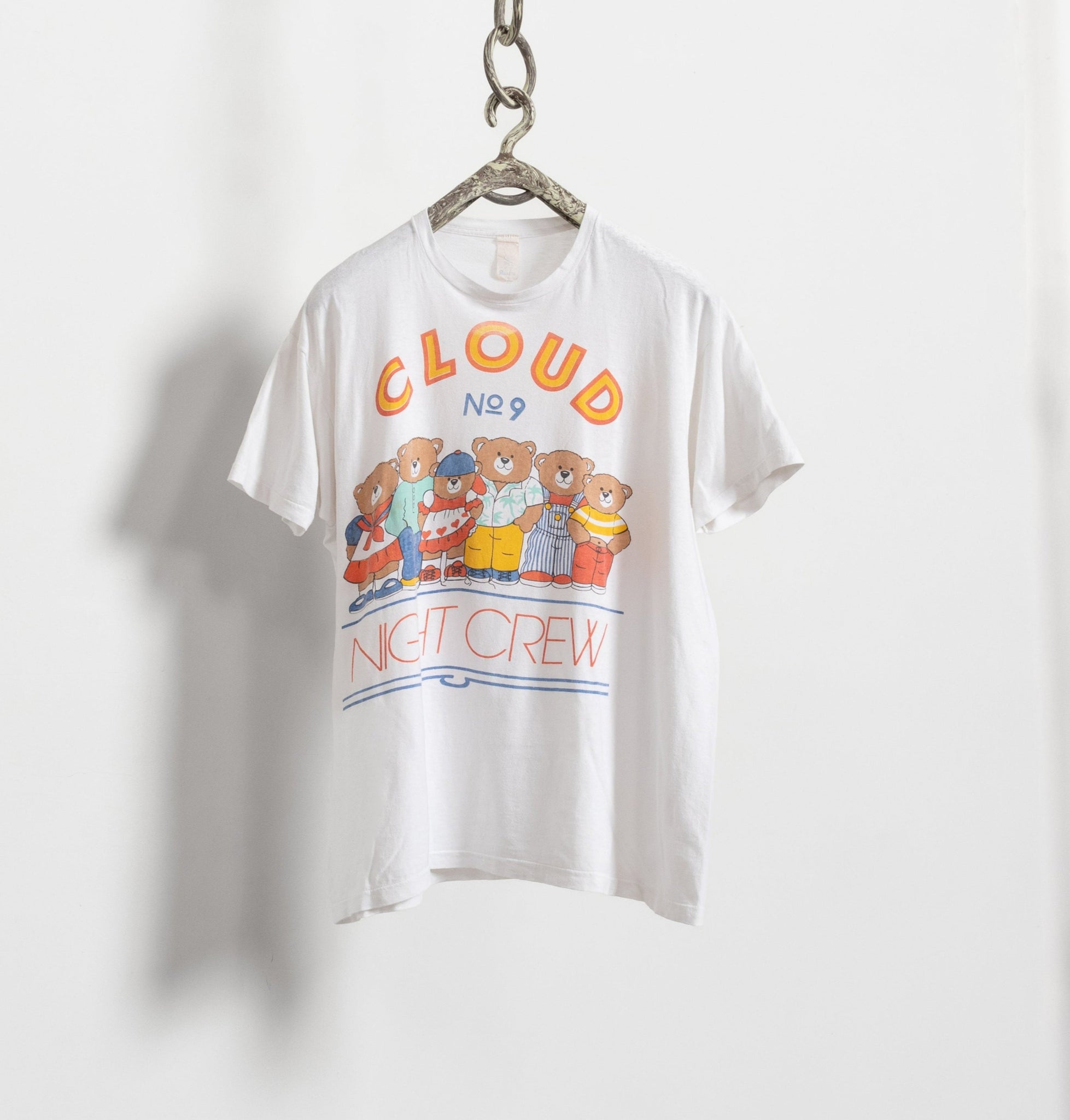 A white vintage 90's cotton-blend t-shirt with a graphic print of teddy bears and the text 'NIGHT CREW', hung on a hanger against a plain background.
