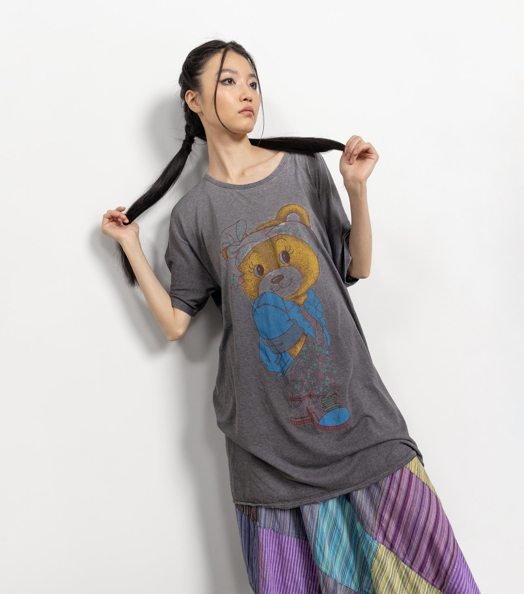 Woman wearing a gray t-shirt with a bear graphic and colorful pants on a white background