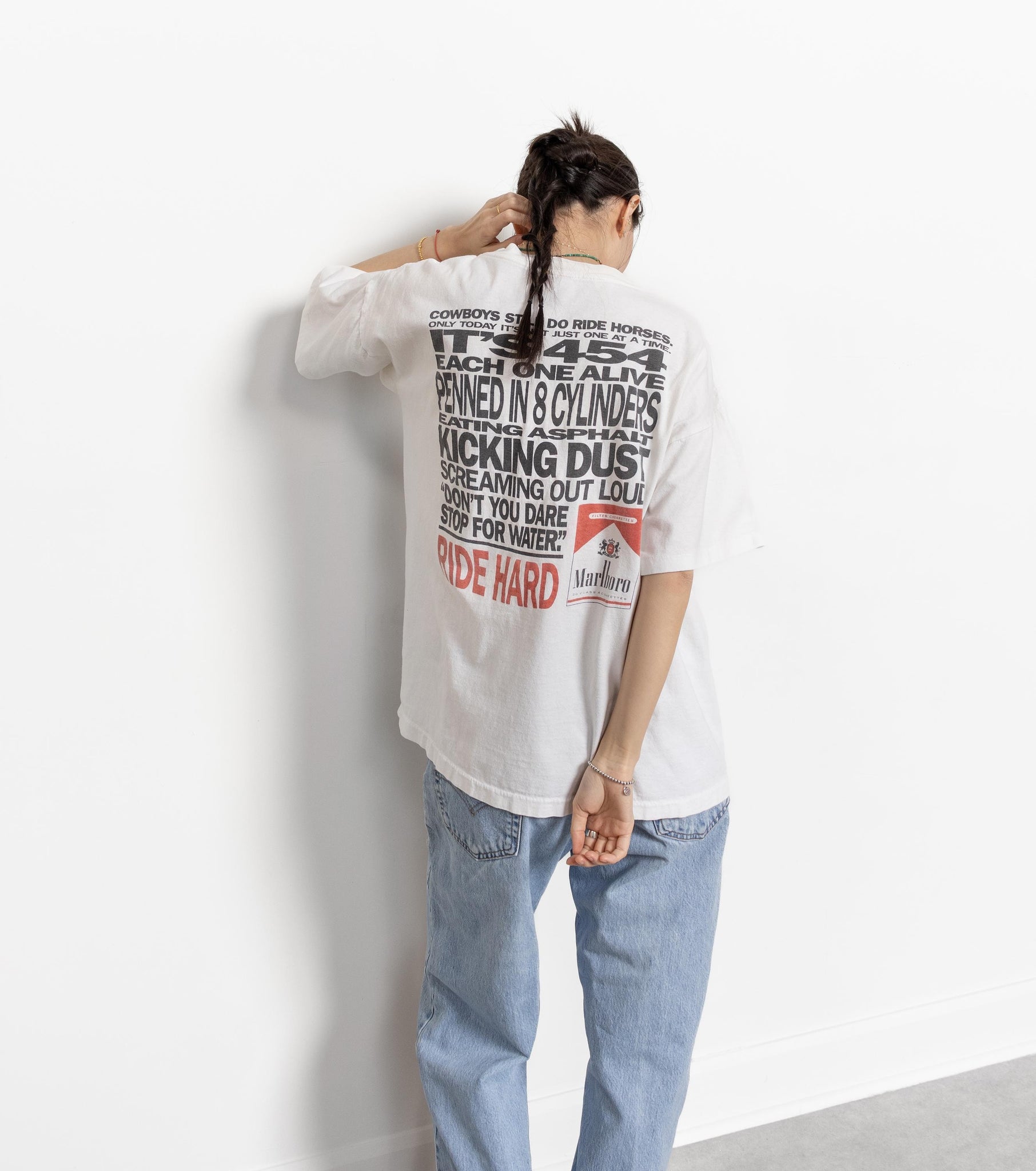 A person wearing a white Marlboro cigarette t-shirt with a large graphic on the back, in front of a plain background.