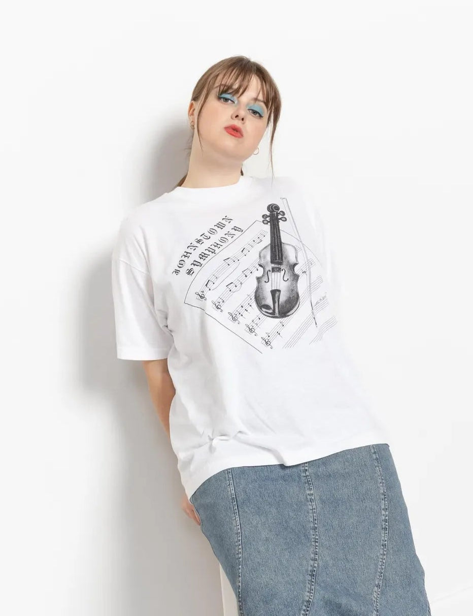 A person wearing a vintage white 50/50 poly cotton violin graphic tee with black boots, sitting against a plain background.