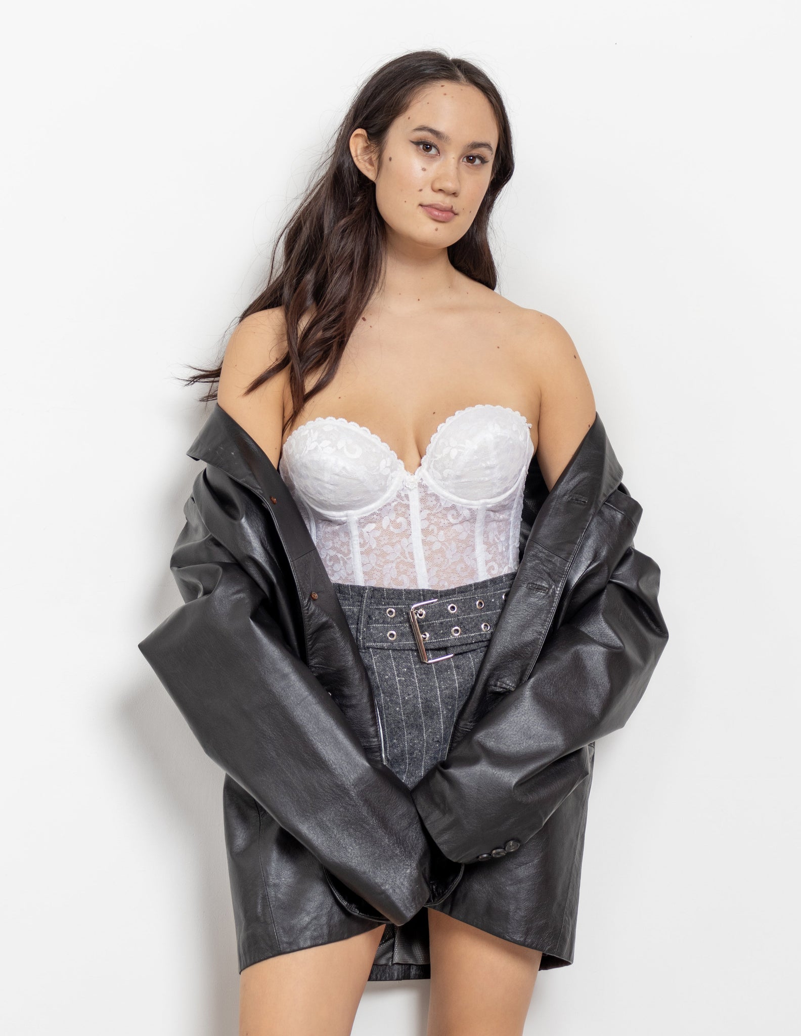 Woman wearing a white lace corset and black leather jacket on a white background