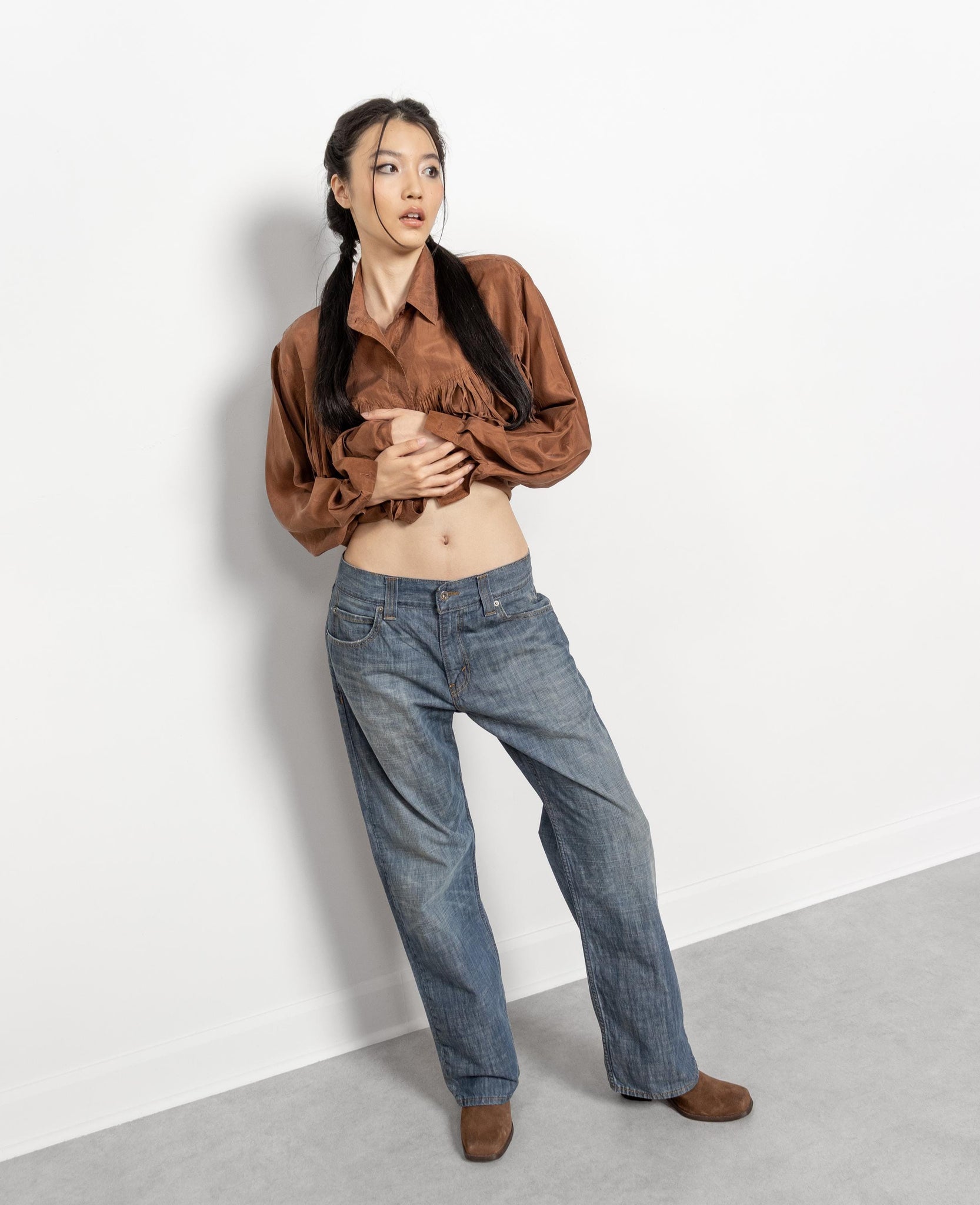 Person wearing a brown shirt and blue jeans against a white background
