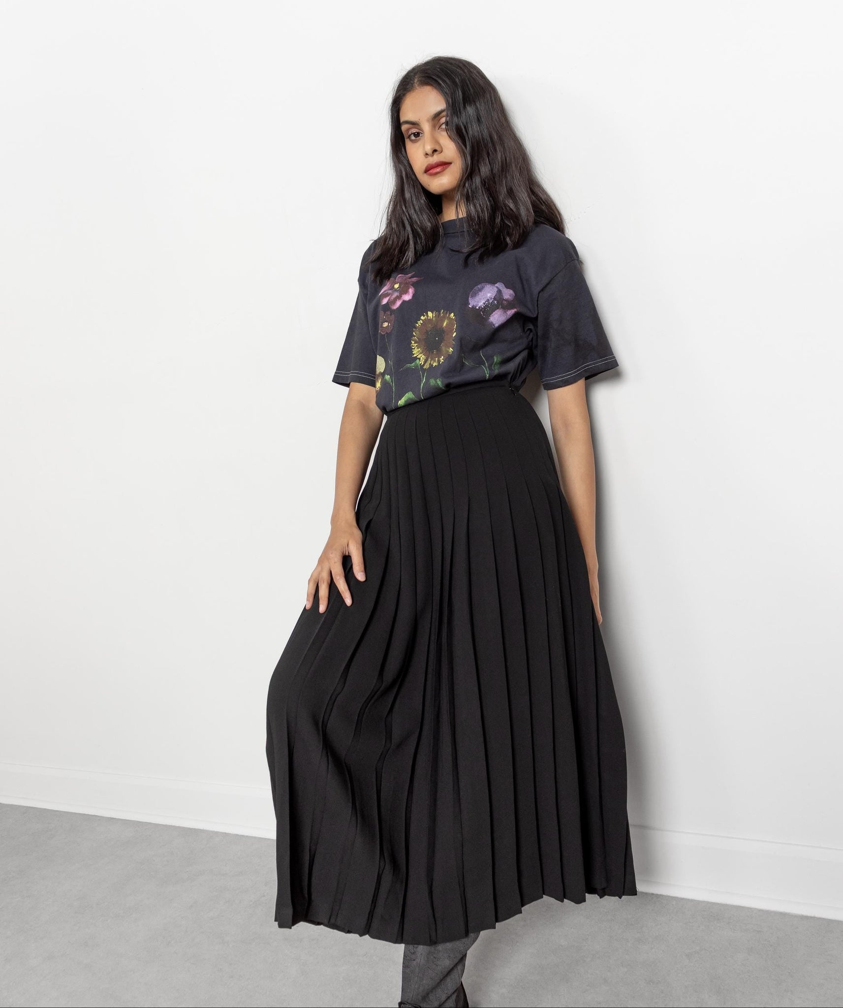 Woman wearing a black pleated skirt with a floral top against a white background