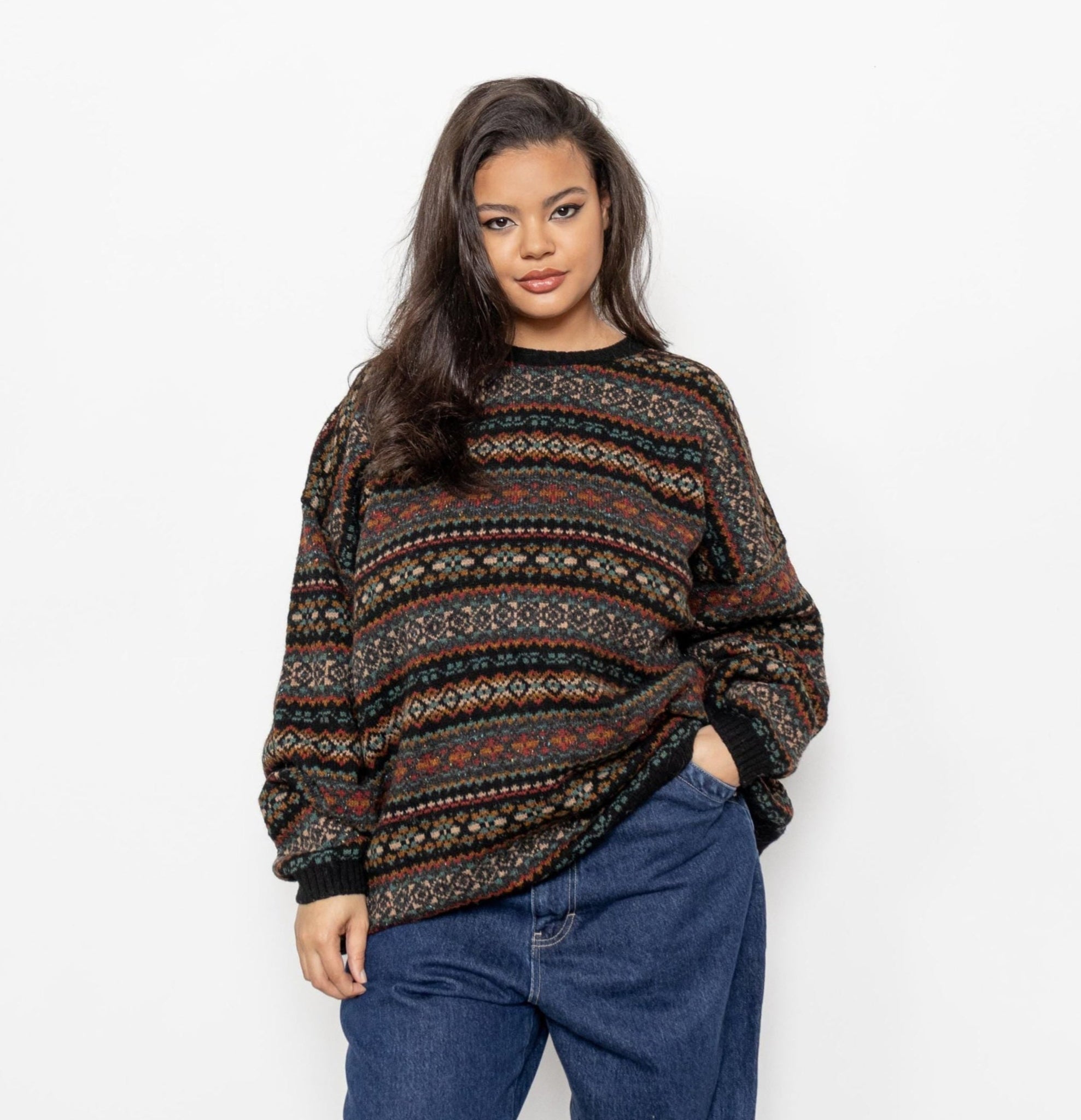 A woman wearing a vintage 90's wool pullover geometric patterned sweater in hues of brown, black, teal, burgundy, and orange, with a crew neck.