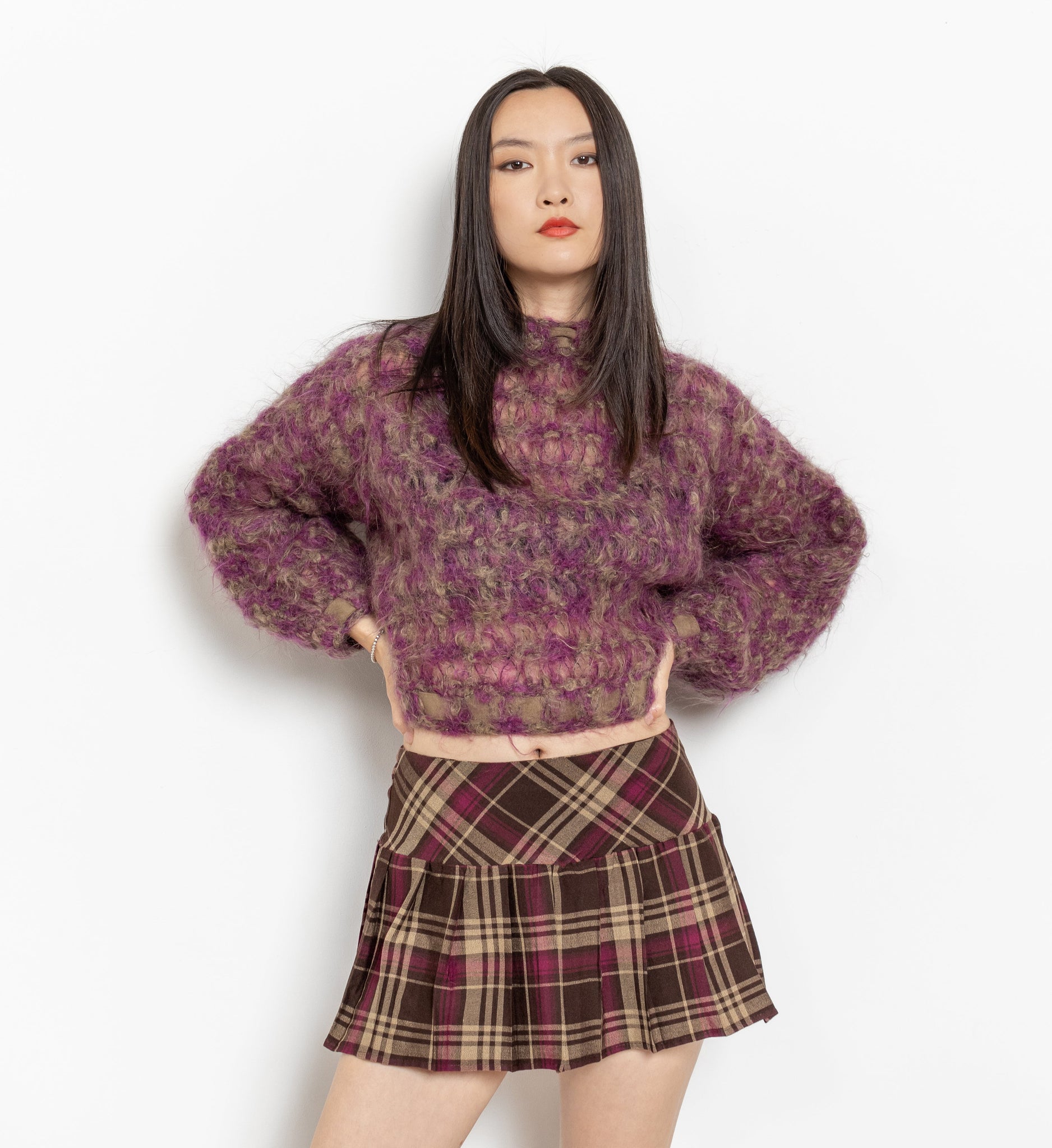 Person wearing a patterned sweater and plaid skirt on a white background