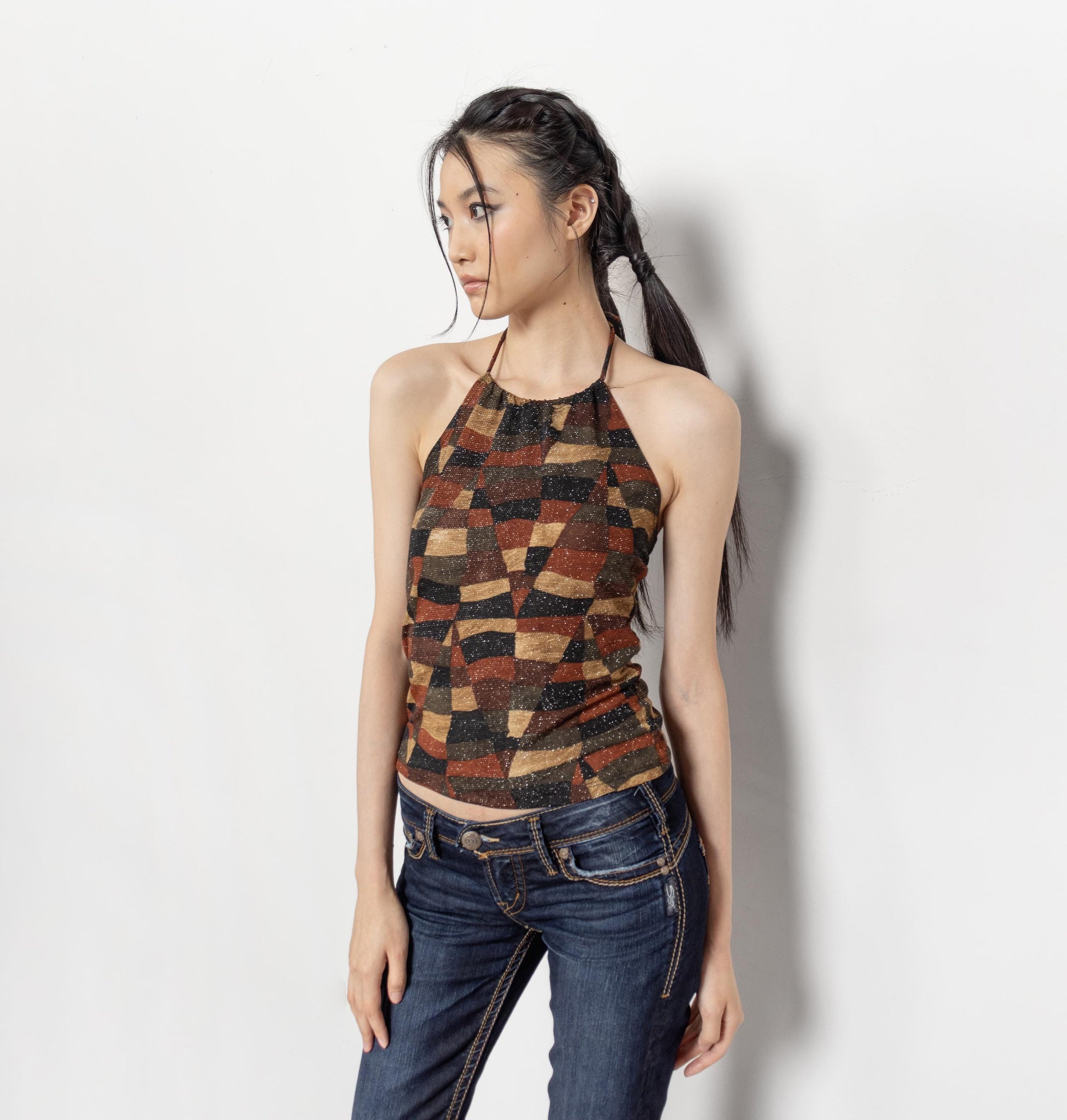 Woman wearing a patterned top and jeans against a white background