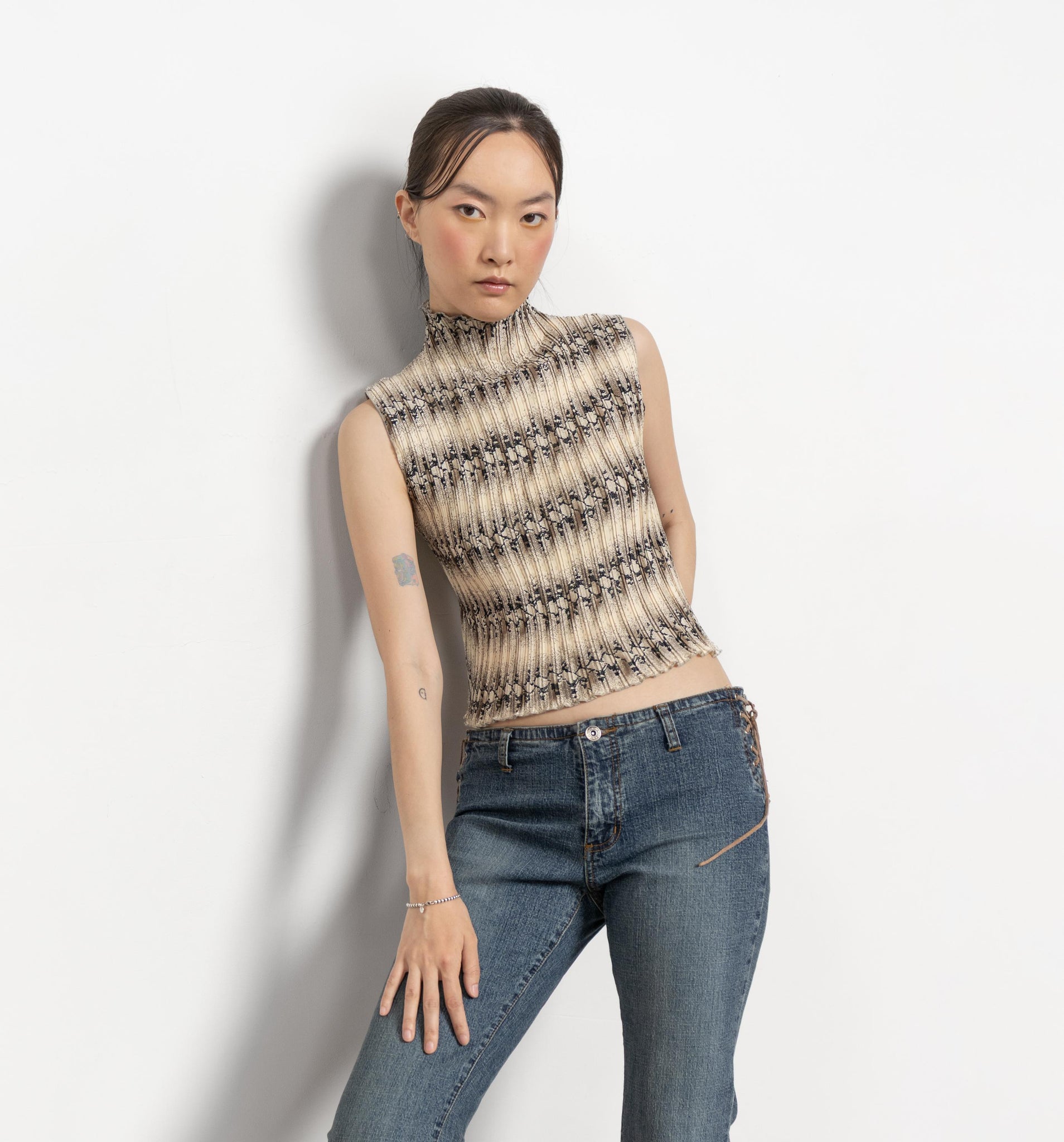 Woman wearing a patterned sleeveless top and blue jeans against a plain background