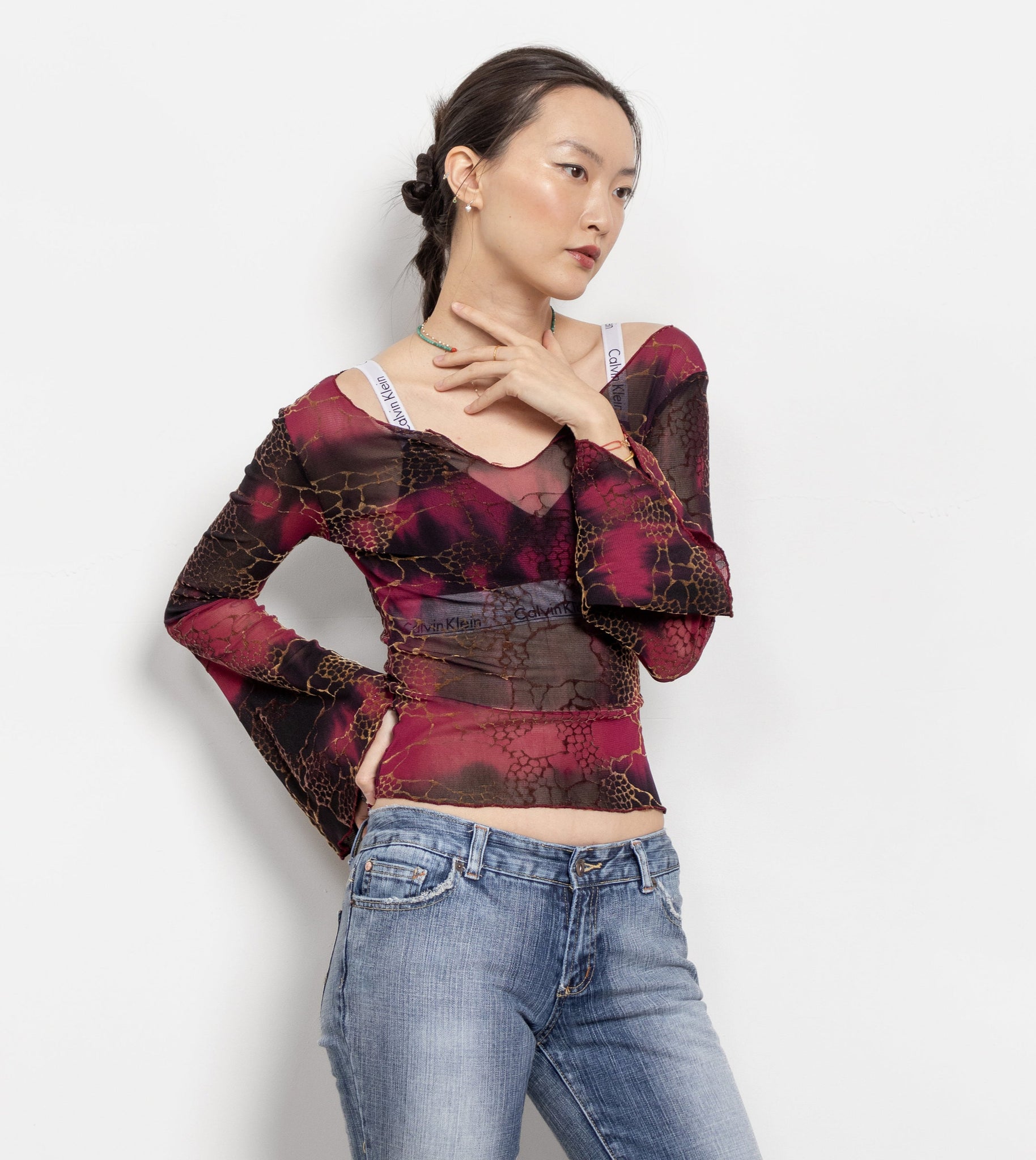 Woman wearing a patterned top and jeans on a white background