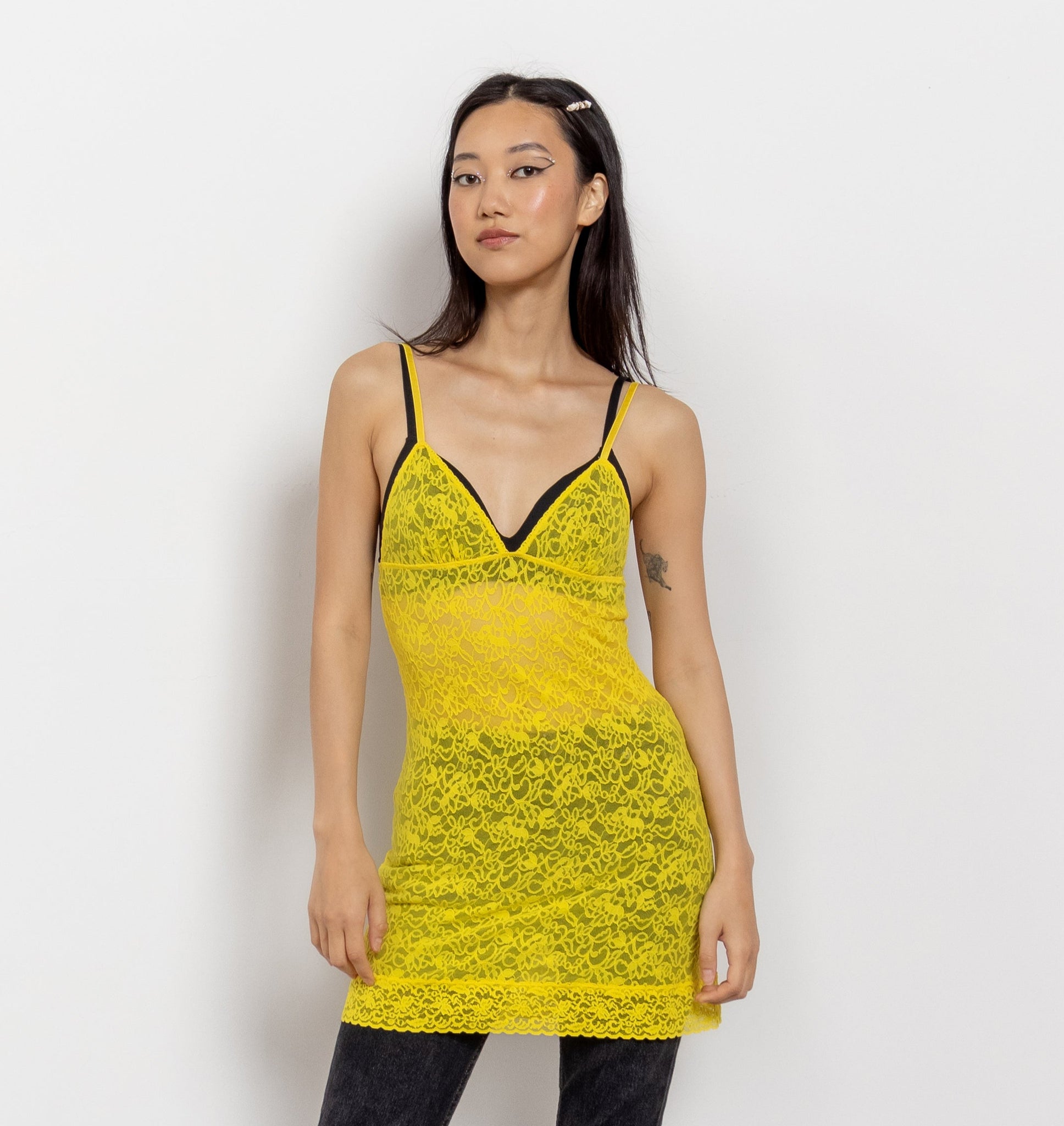 Woman wearing a yellow lace dress and black pants on a white background