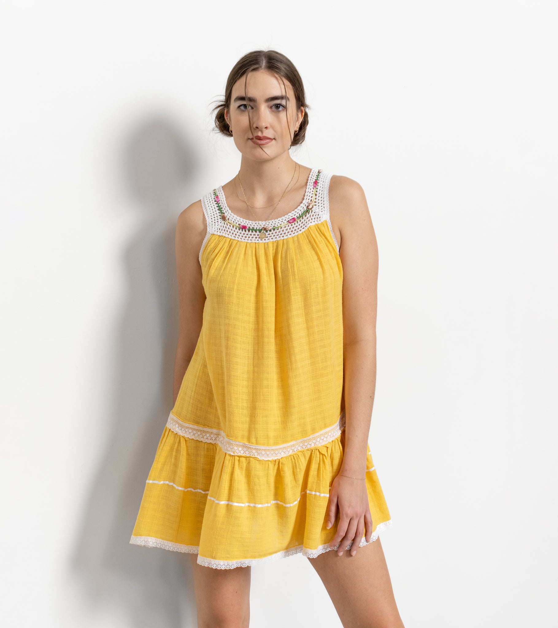 A vintage sleeveless yellow gauze mini dress with a scoop neckline and white crochet band, embroidered roses, and a slight uneven hem.