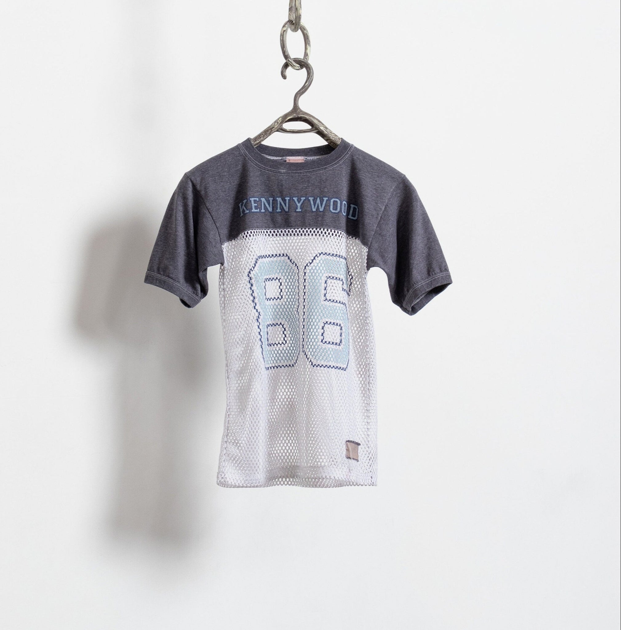 A vintage gray and white Kennywood theme park t-shirt with the number 86 and text on the back, hanging against a white wall.