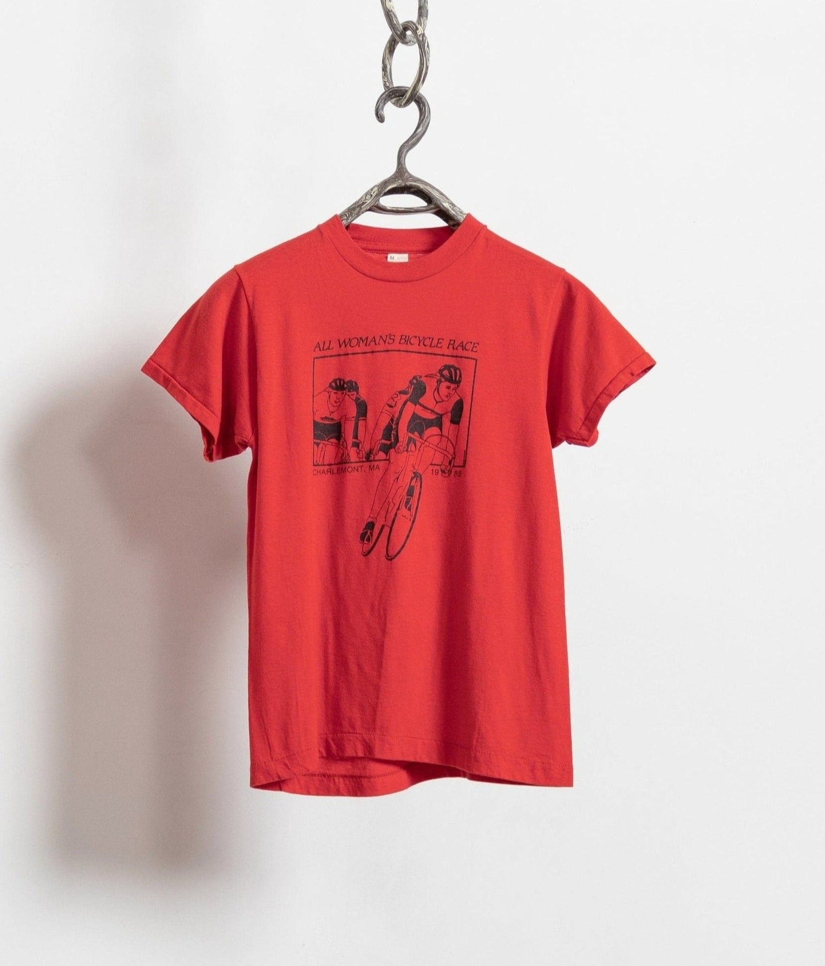 A red vintage cycling t-shirt with a graphic print, hanging against a white background.