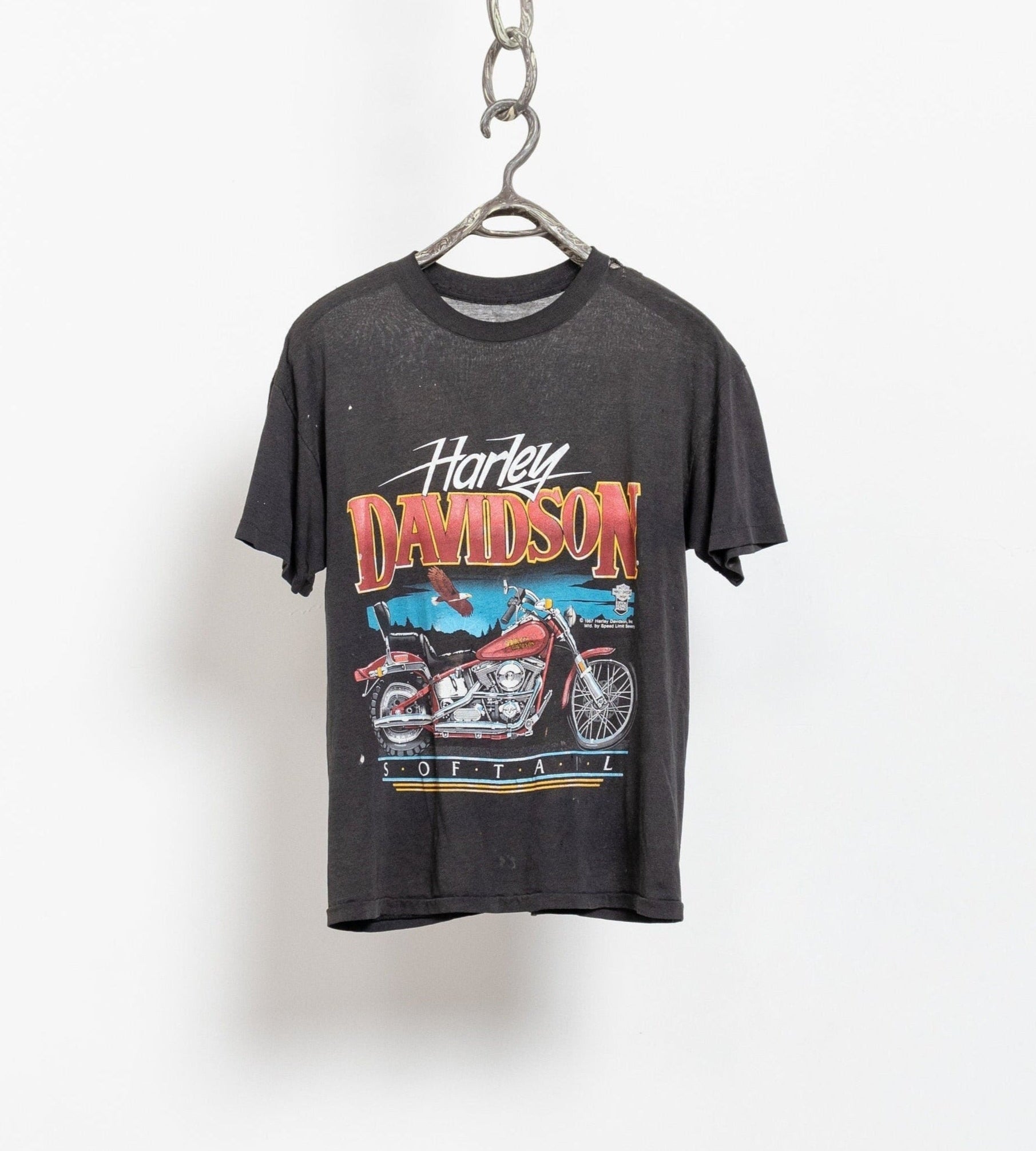 A vintage 80's Harley Davidson short sleeve tee with graphic print of a motorcycle, hanging on a white background.