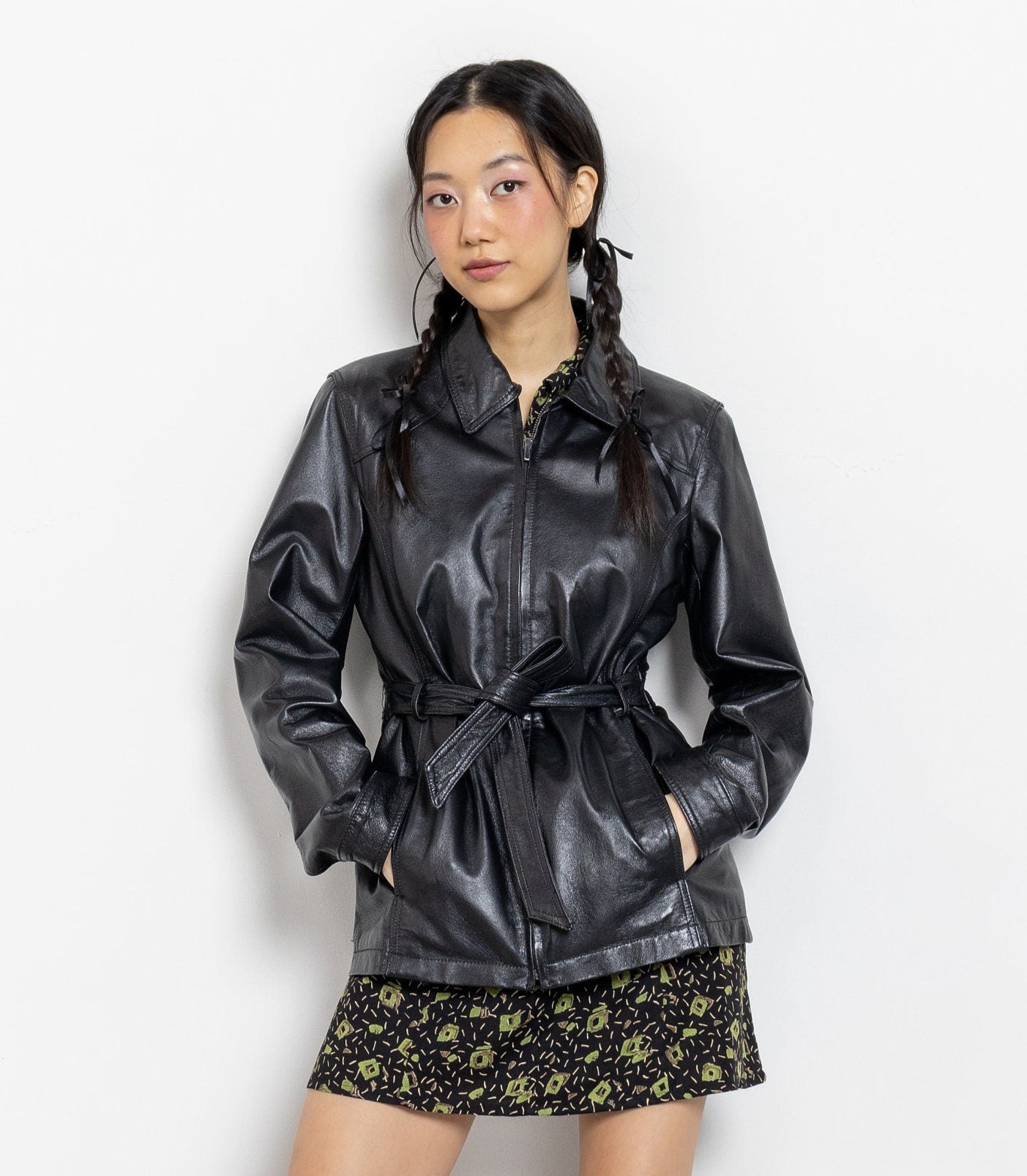 Person wearing a black leather jacket and skirt with black boots on a white background