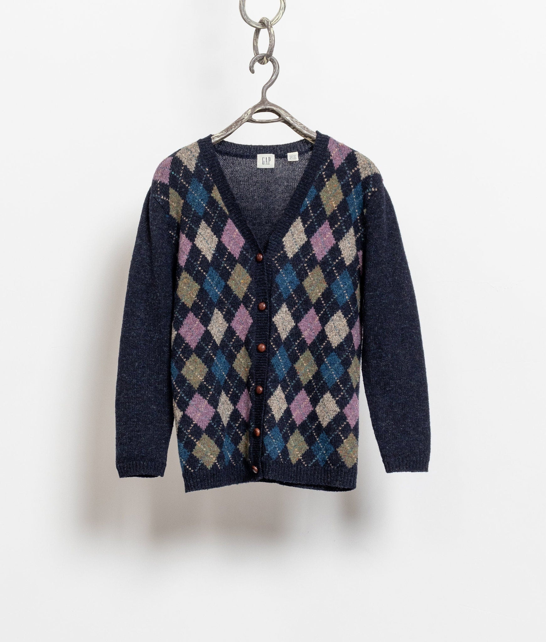 A vintage 90's navy, blue, purple, and brown argyle pattern wool cardigan hanging on a hanger, with wooden buttons visible.