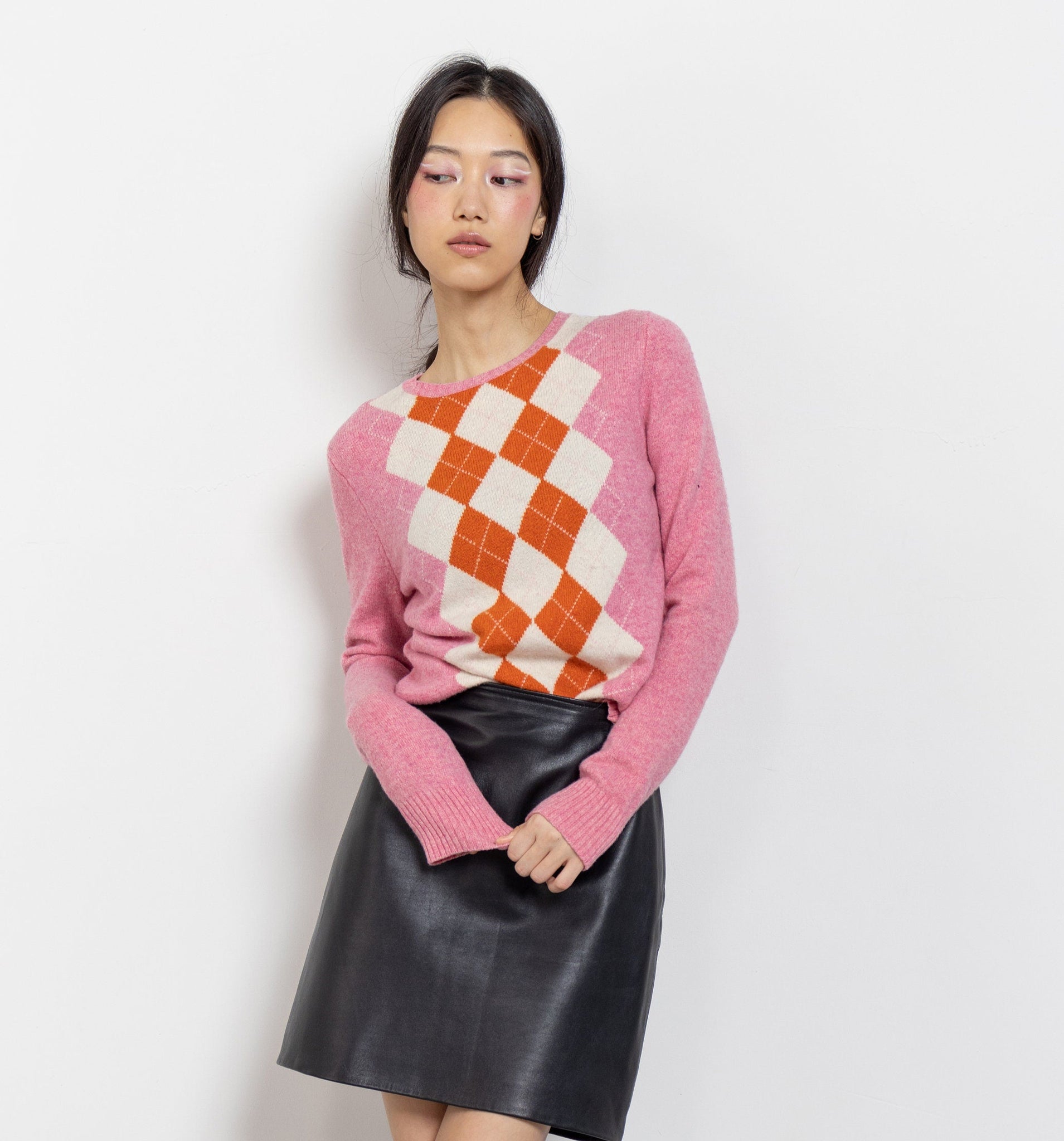 Person wearing a pink sweater with a checkered pattern, black leather skirt, and black knee-high boots on a white background
