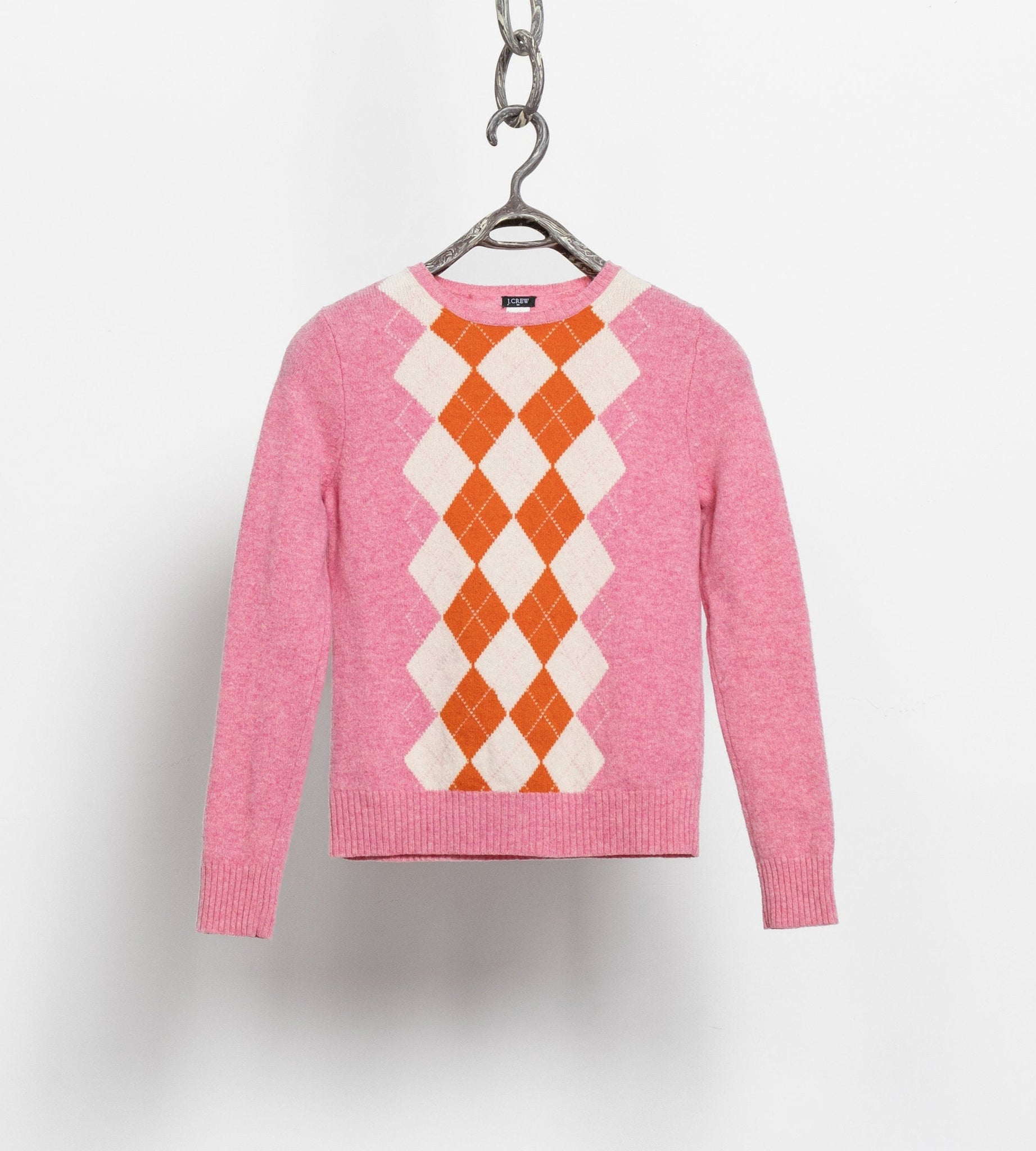 A pink, orange, and white argyle patterned pullover sweater with a crew neckline, hanging against a white background.