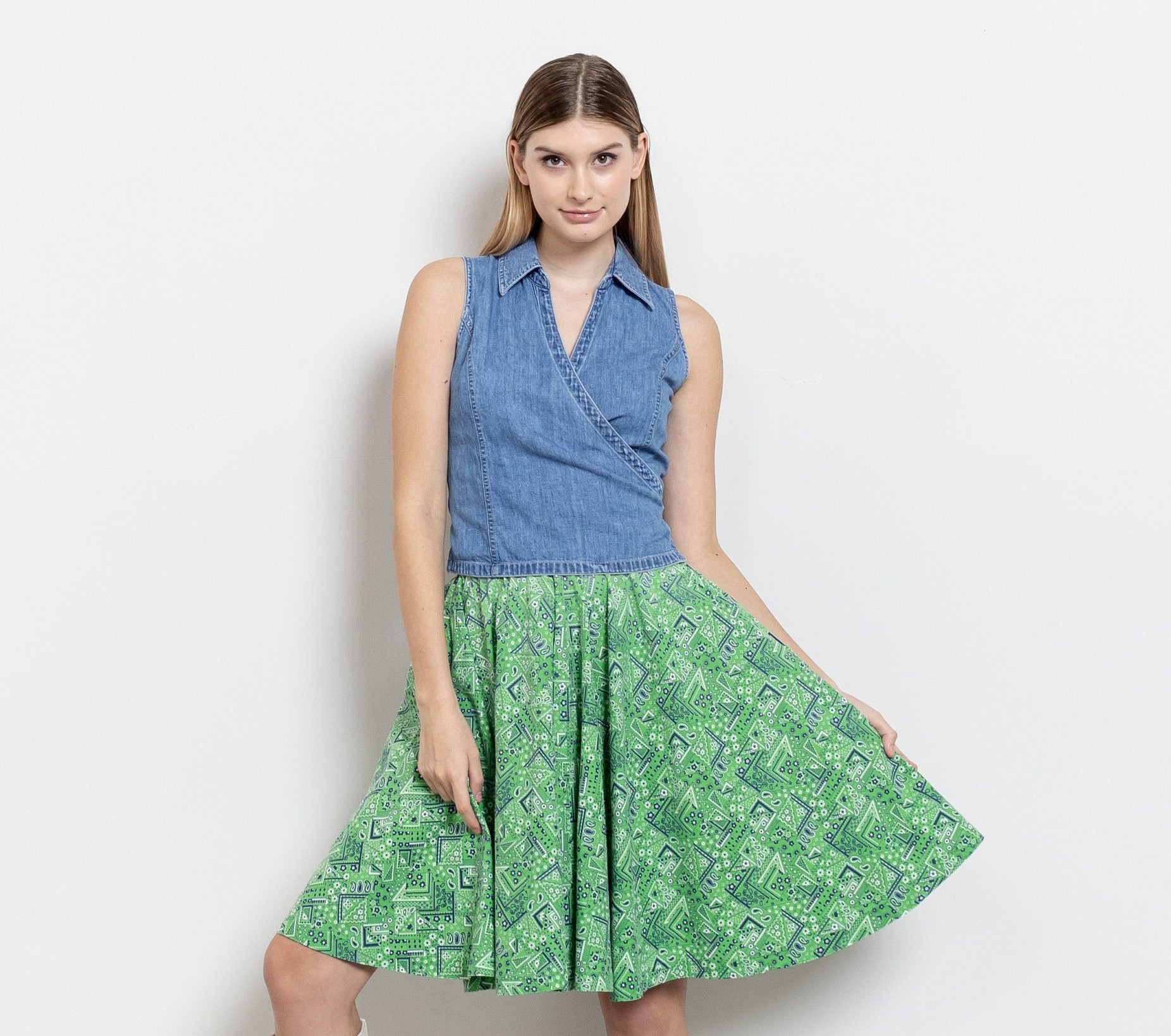 Woman wearing a blue sleeveless top and green floral skirt with white boots on a plain background