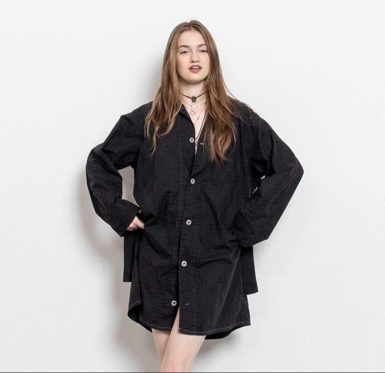 A person wearing an oversized vintage black dress shirt with a button down front and a matching waist tie.