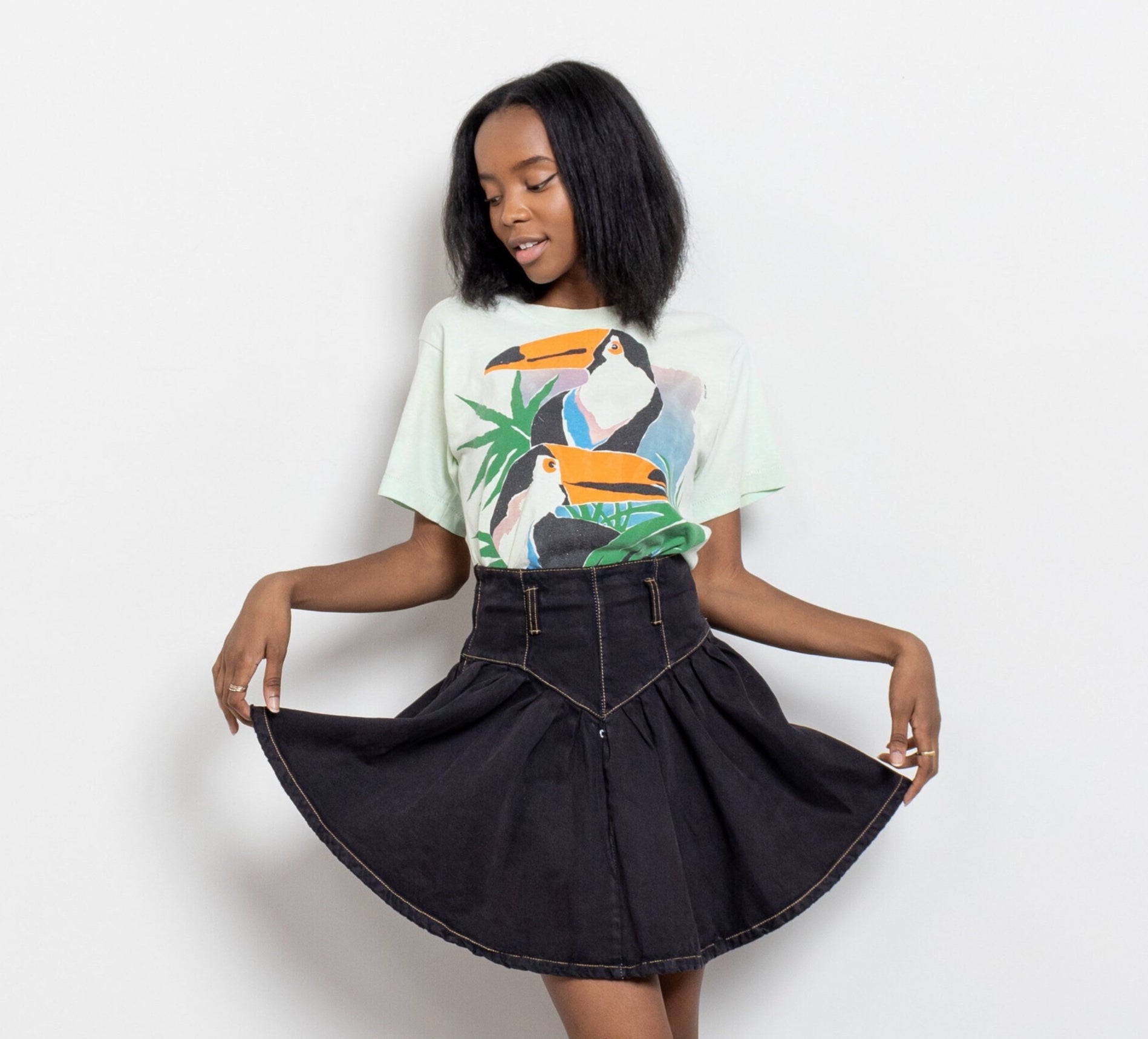 Woman wearing a graphic t-shirt, black skirt, and brown boots on a white background